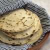 a stack of chickpea and cassava tortillas wrapped in a kitchen towel are resting in a tortilla warmer with the lid removed