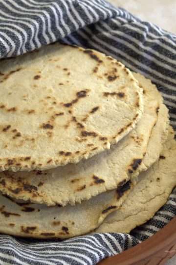 a stack of chickpea and cassava tortillas wrapped in a kitchen towel are resting in a tortilla warmer with the lid removed