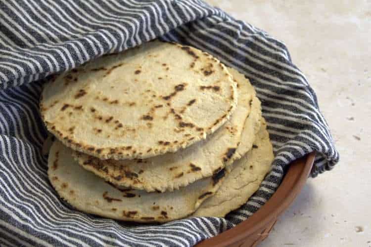 a stack of chickpea and cassava tortillas wrapped in a kitchen towel are resting in a tortilla warmer with the lid removed