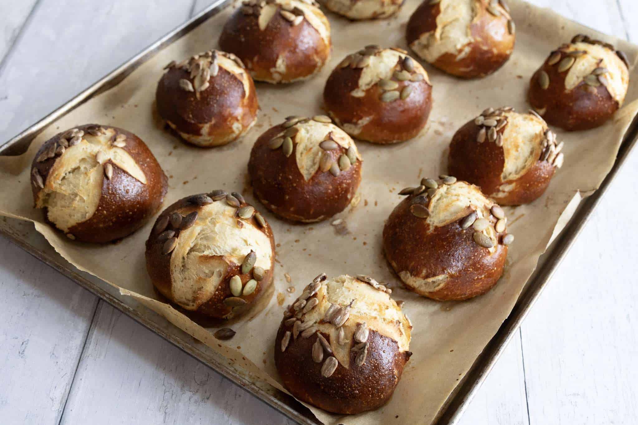 A batch of beautifully dark brown and freshly baked sourdough pretzel rolls on a parchment lined baking sheet