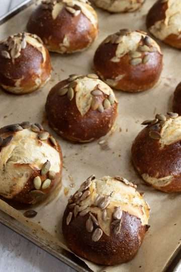a parchment lined baking sheet holding pretzel rolls is resting on a white wood surface