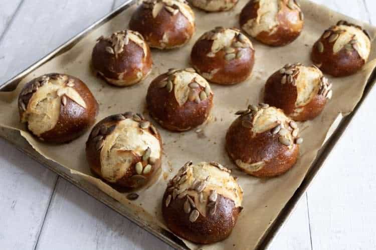 a parchment lined baking sheet holding pretzel rolls is resting on a white wood surface
