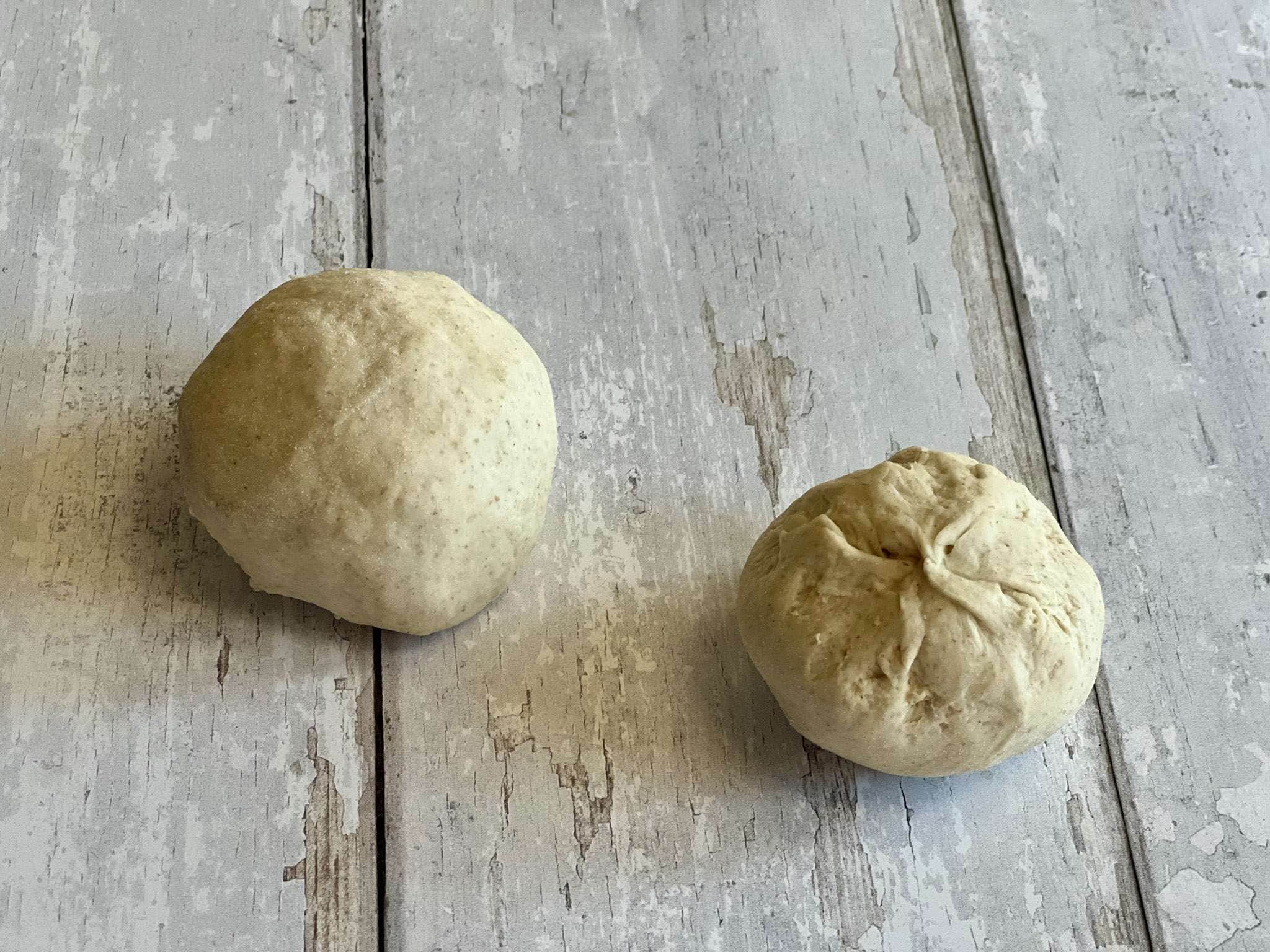 Two shaped balls of dough for sourdough pretzel rolls, one seam side down and one seam side up, are shown on a white wood look surface