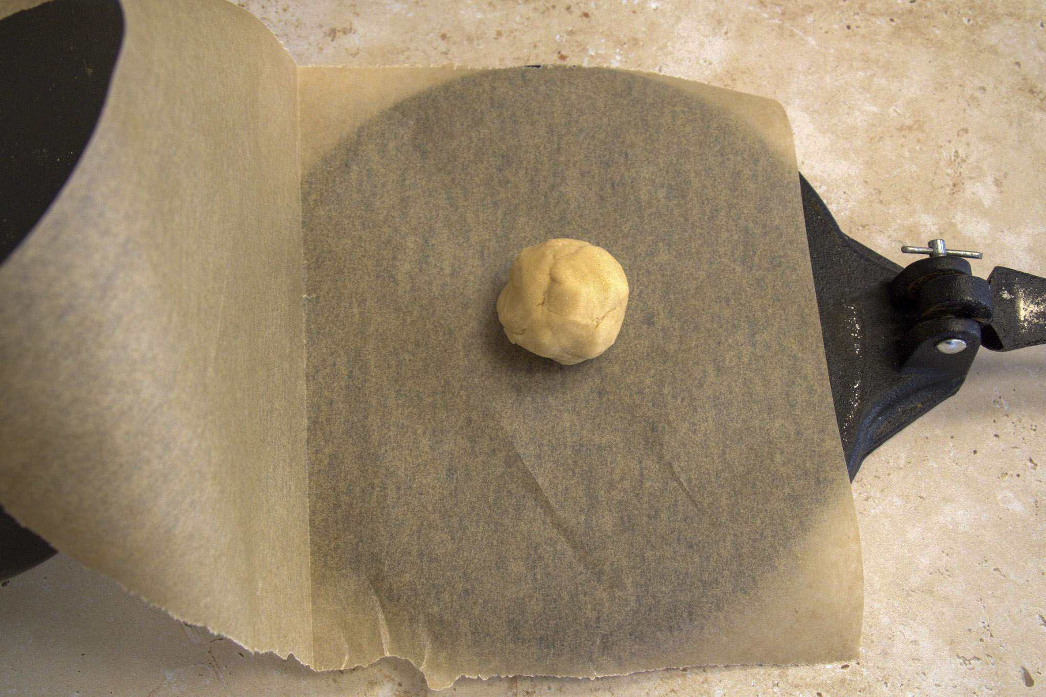 a ball of chickpea and cassava tortilla dough on a tortilla press between pieces of parchment paper