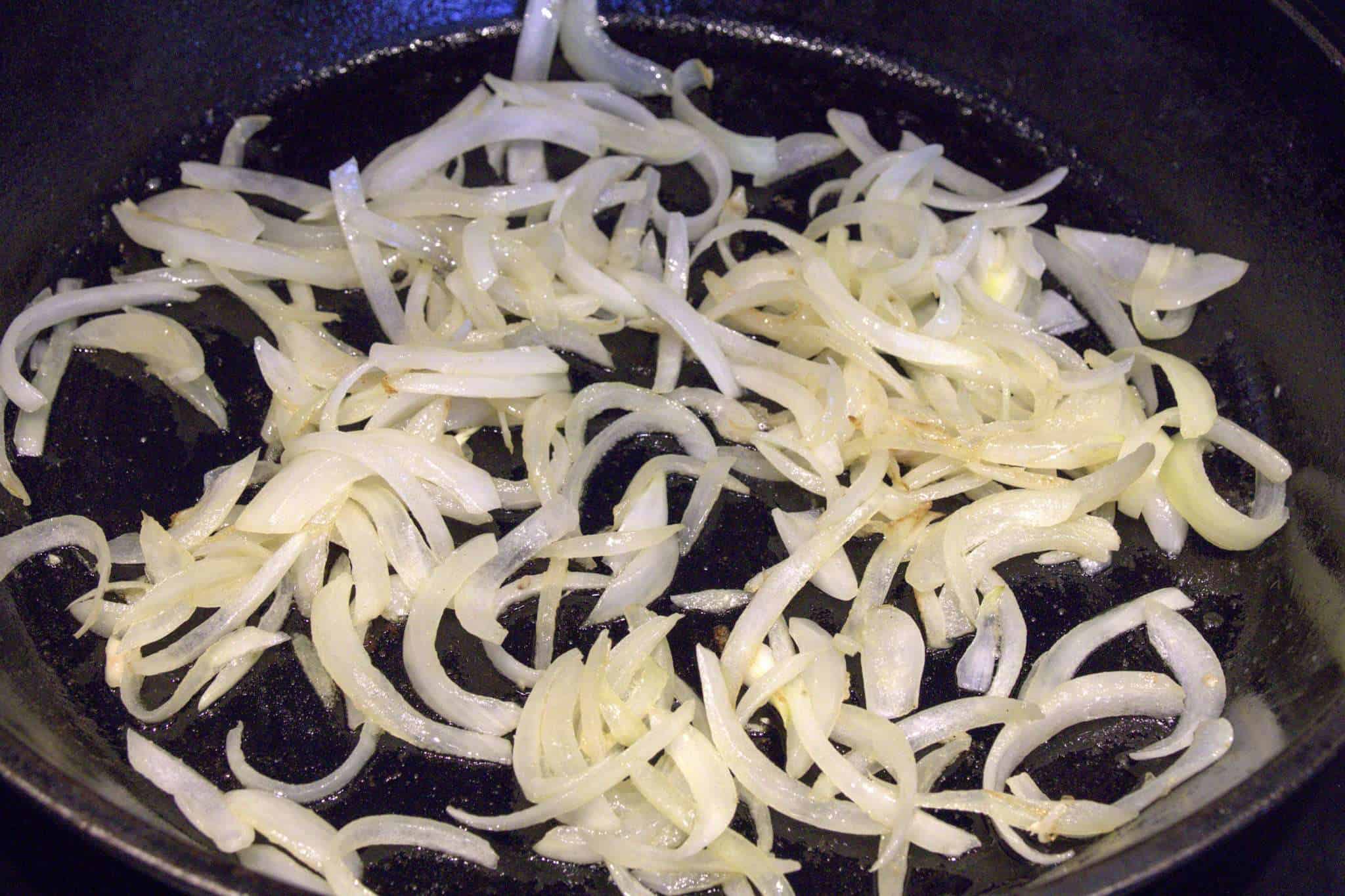 onions for adobo-inspired chicken and kale tacos sauteeing in a cast iron pan