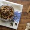 a glass jar with rhubarb chutney is resting on a white and blue kitchen towel, which is resting on a wooden surface - a piece of ginger and 3 cinnamon sticks are in the picture and a couple pieces of star anise are resting on the kitchen towel