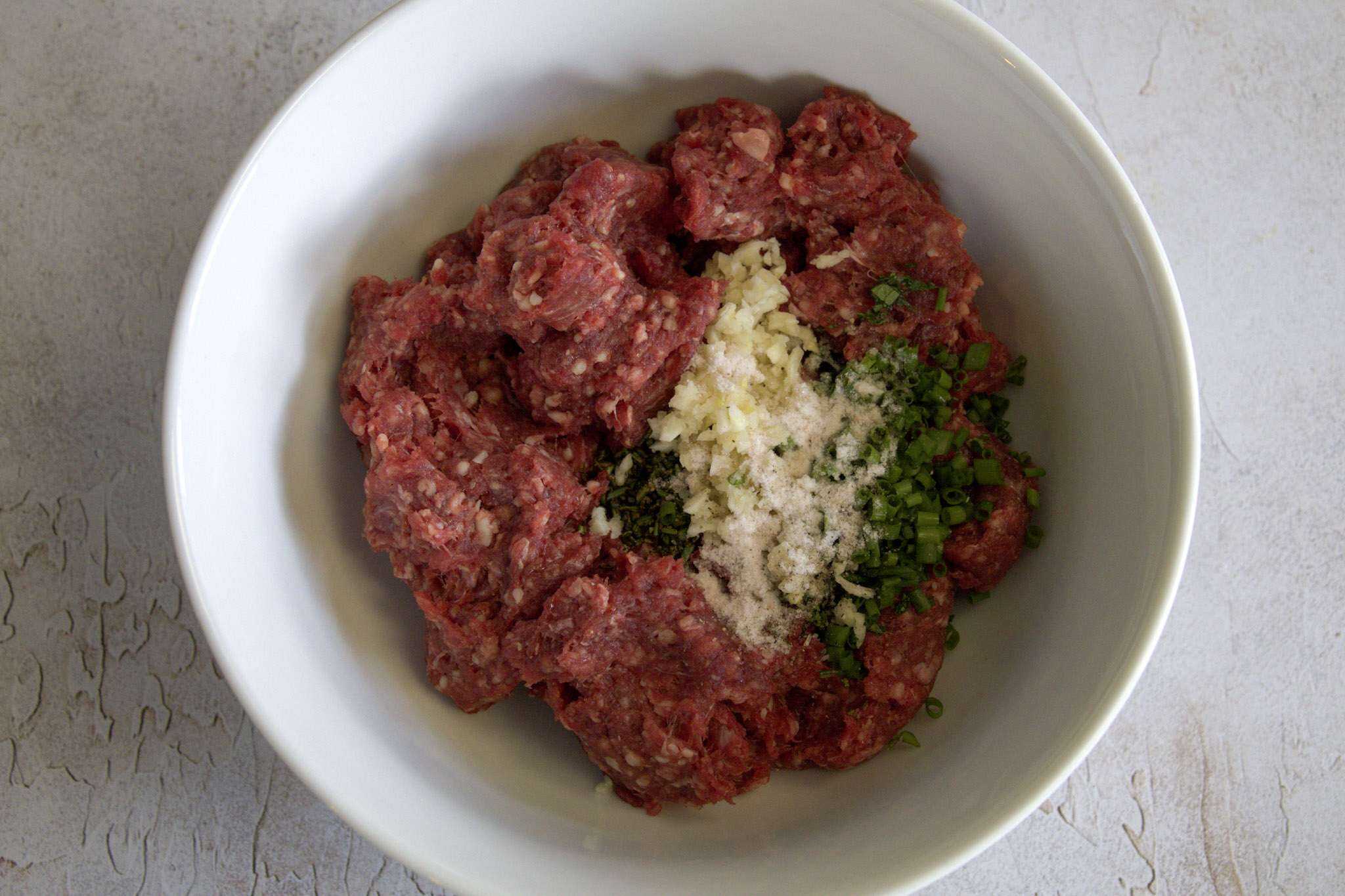 w white bowl with ground bison, herbs and garlic ready to be mixed together
