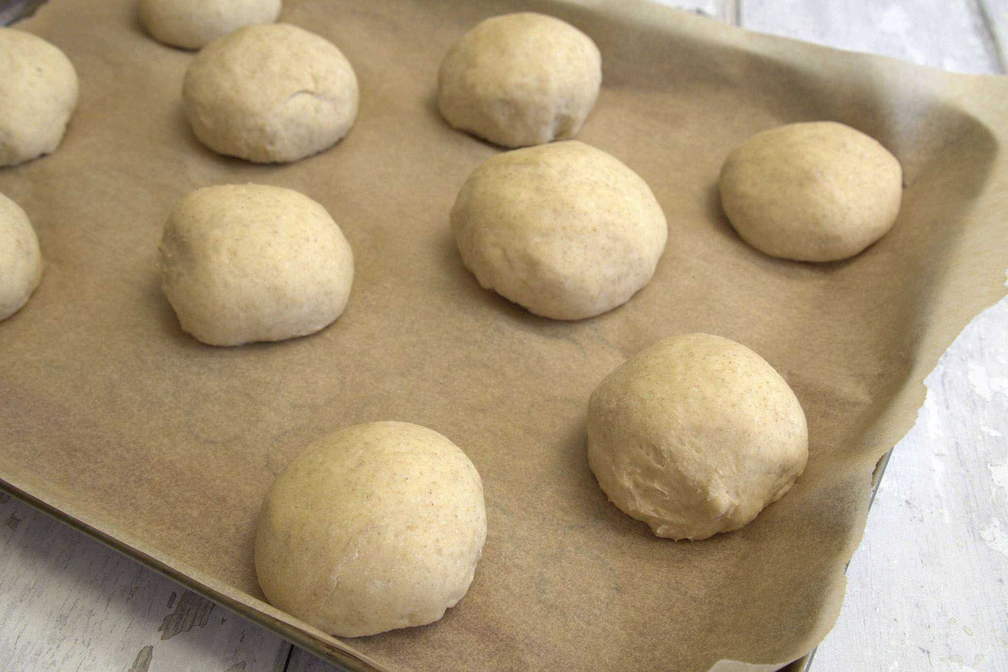 Shaped and unbaked sourdough pretzel rolls on a parchment lined baking sheet