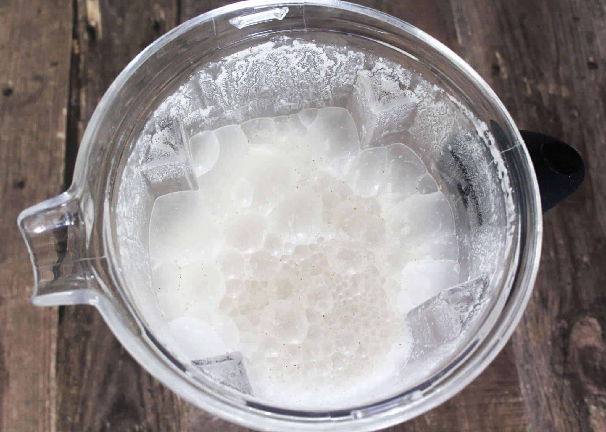 A blender container with foamy blended nut milk on a wooden surface