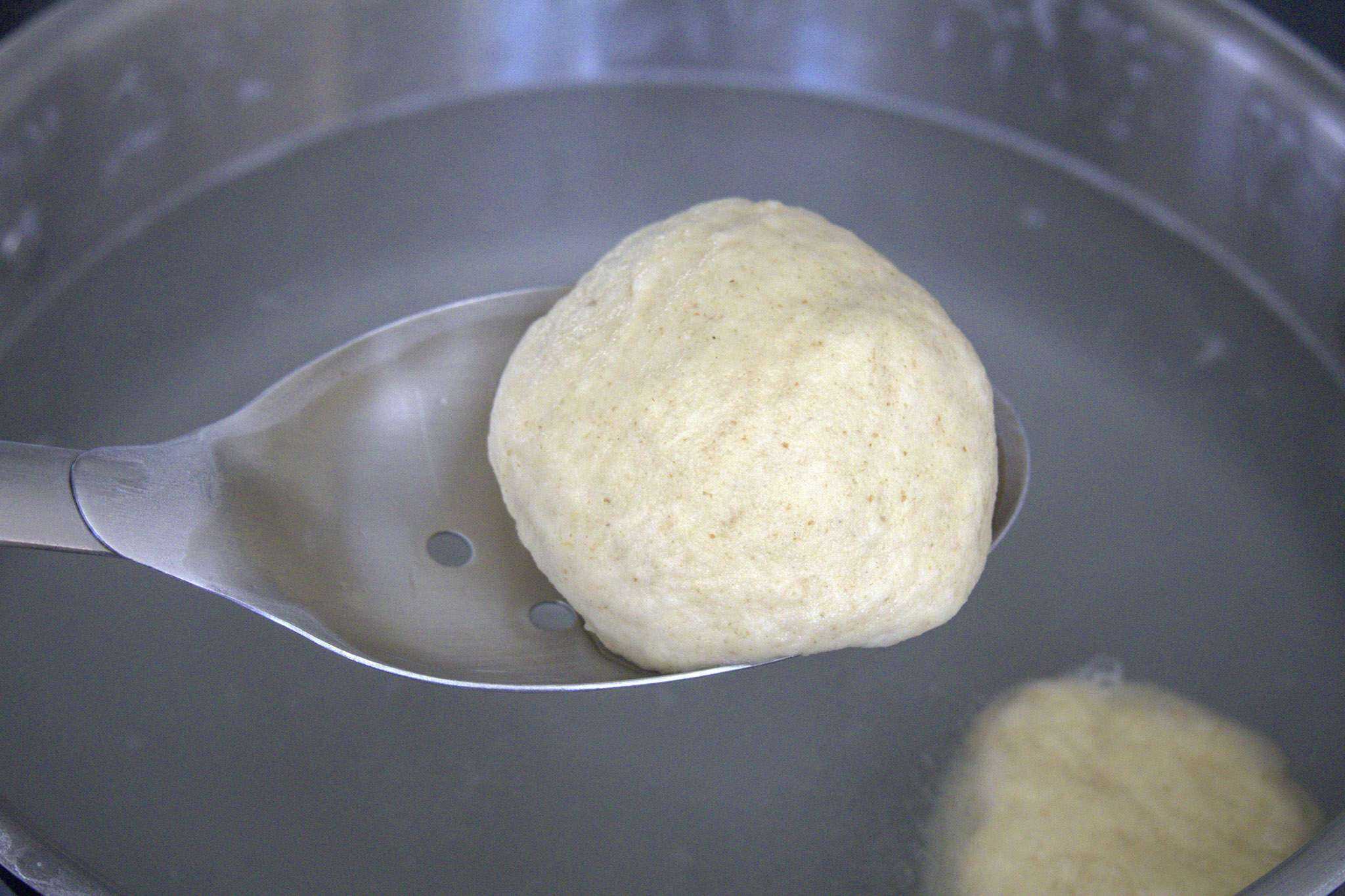A just boiled sourdough pretzel roll is resting in a slotted spoon