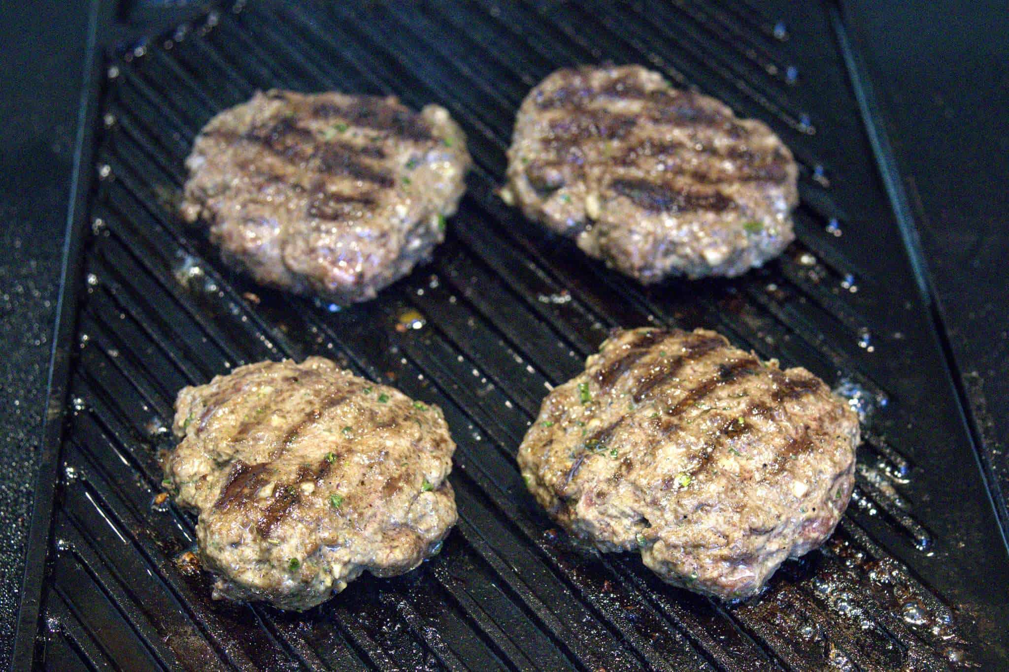 4 bison burger patties are cooking on a grill pan