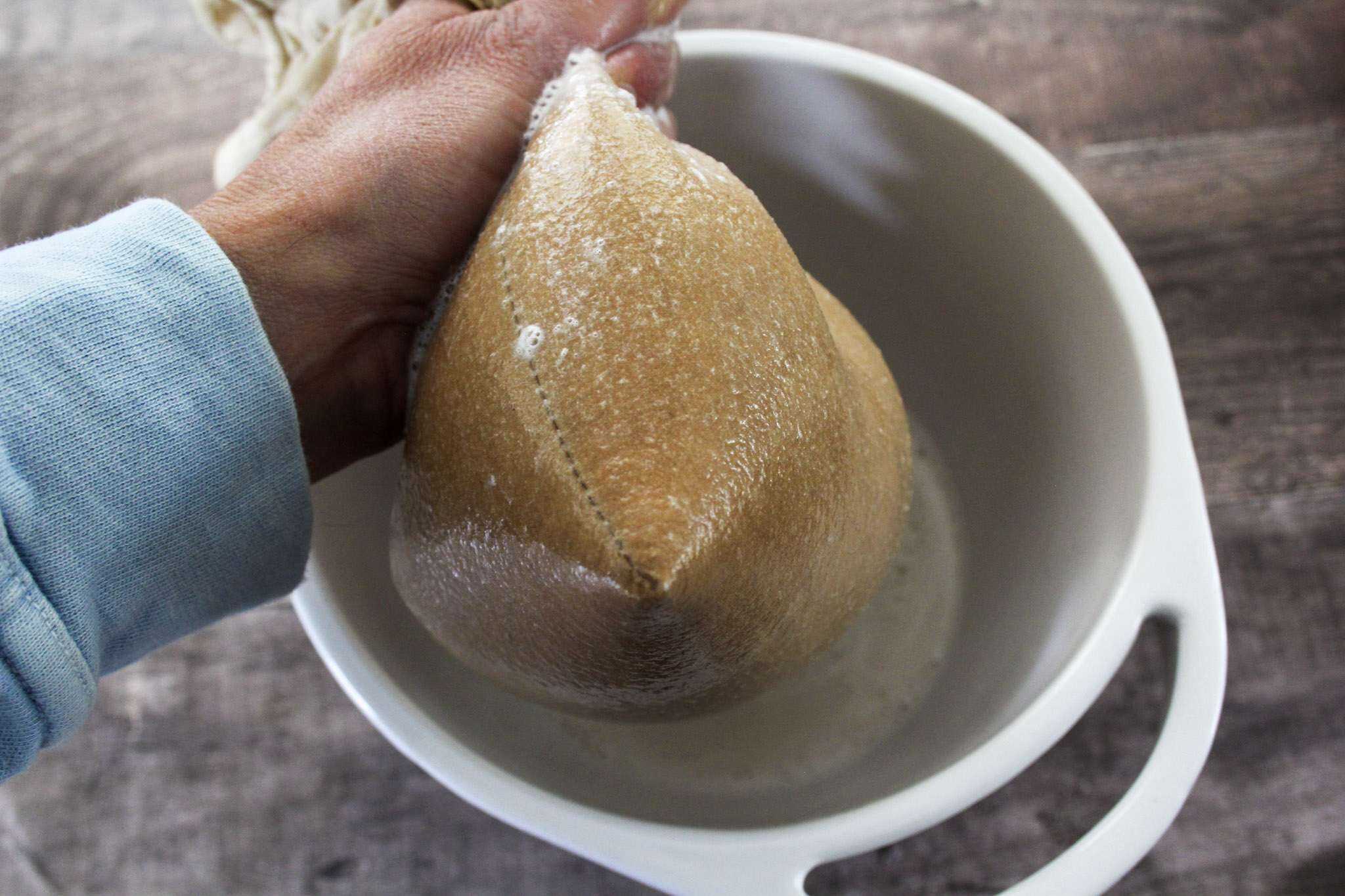 a white bowl is shown and a person's hand can be seen holding a full nut milk bag