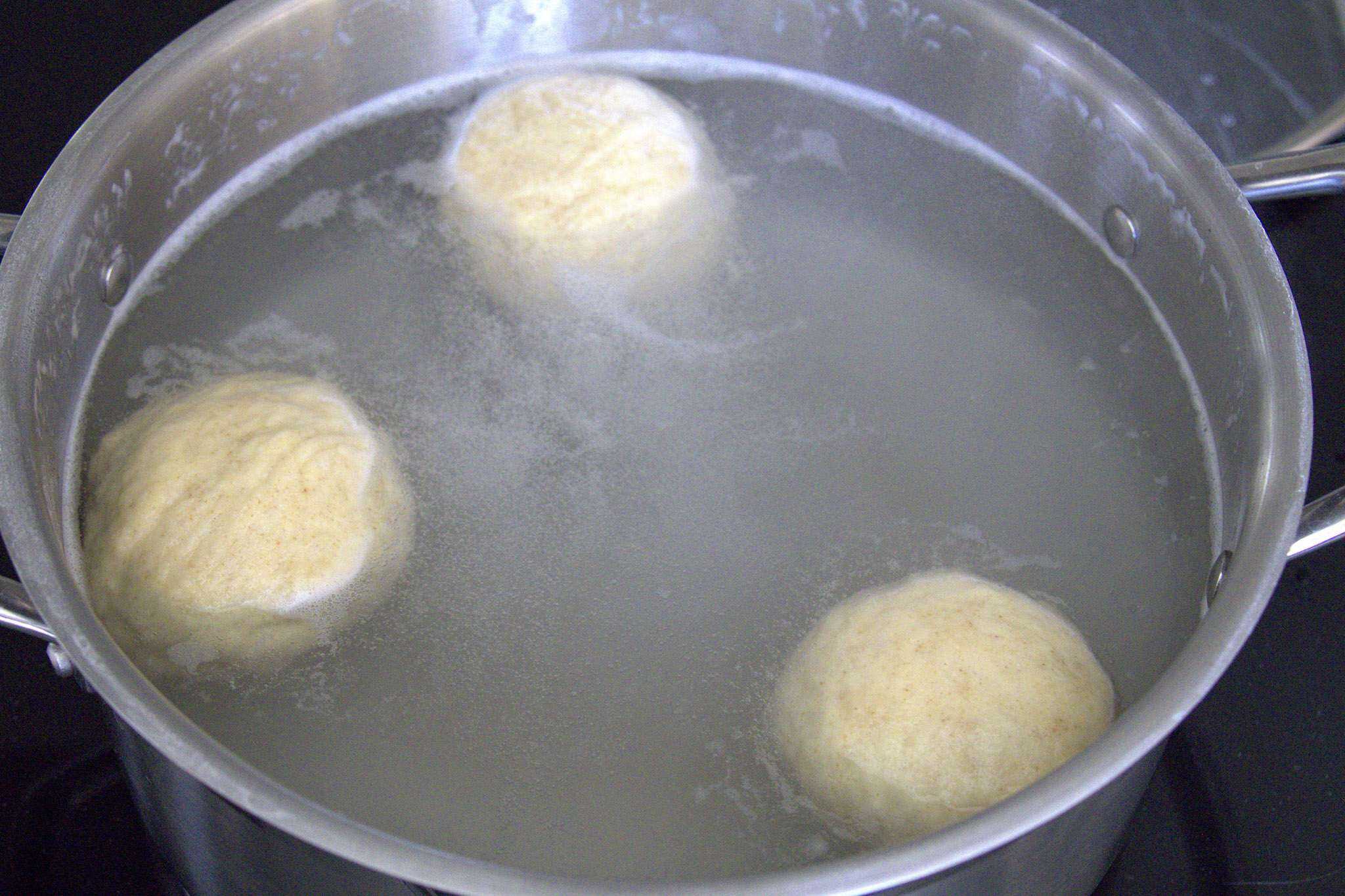 3 sourdough pretzel rolls are boiling in a pot with baking soda water