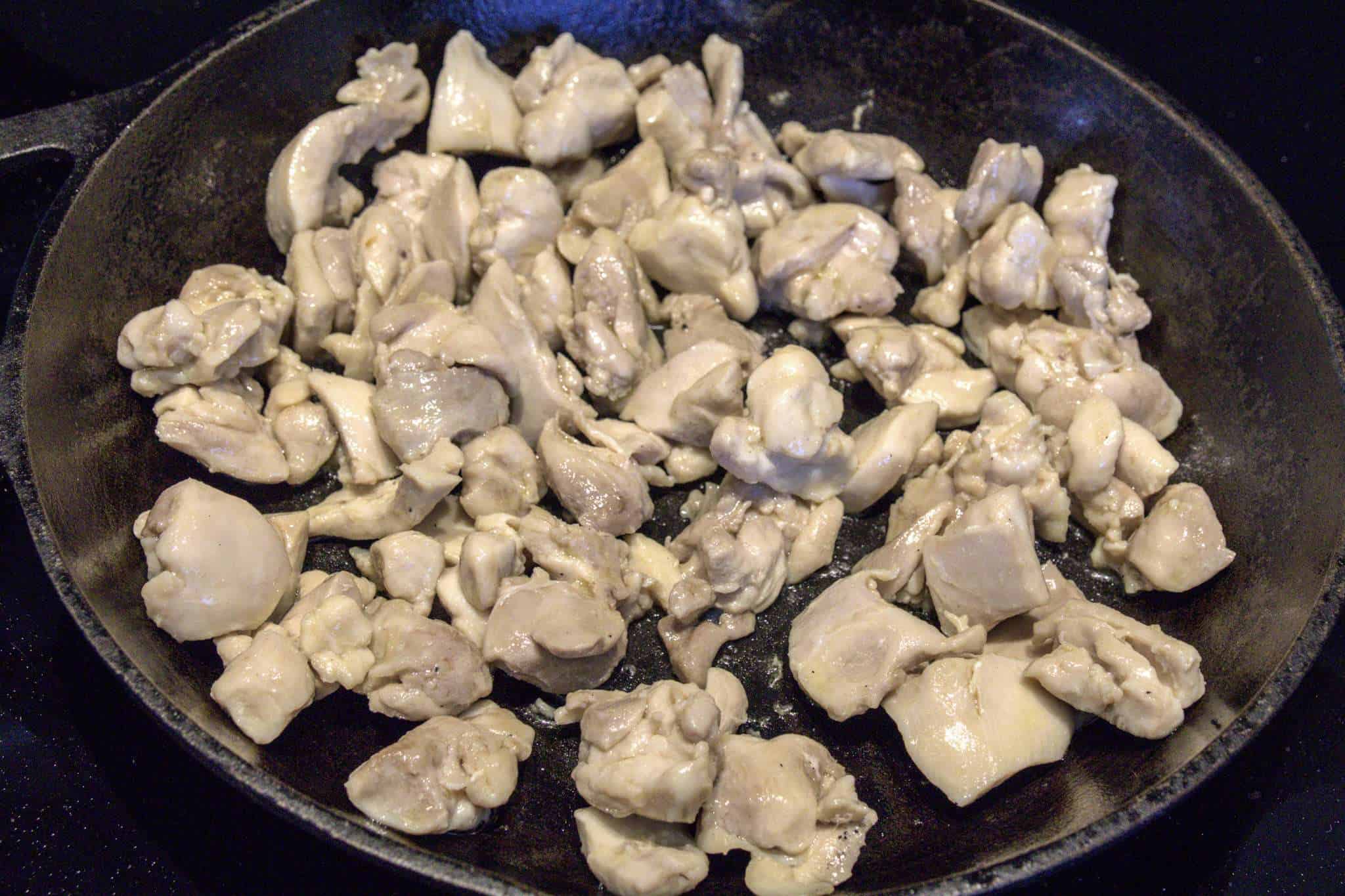 bite-sized chicken pieces for adobo-inspired chicken and kale tacos sauteeing in a cast iron pan