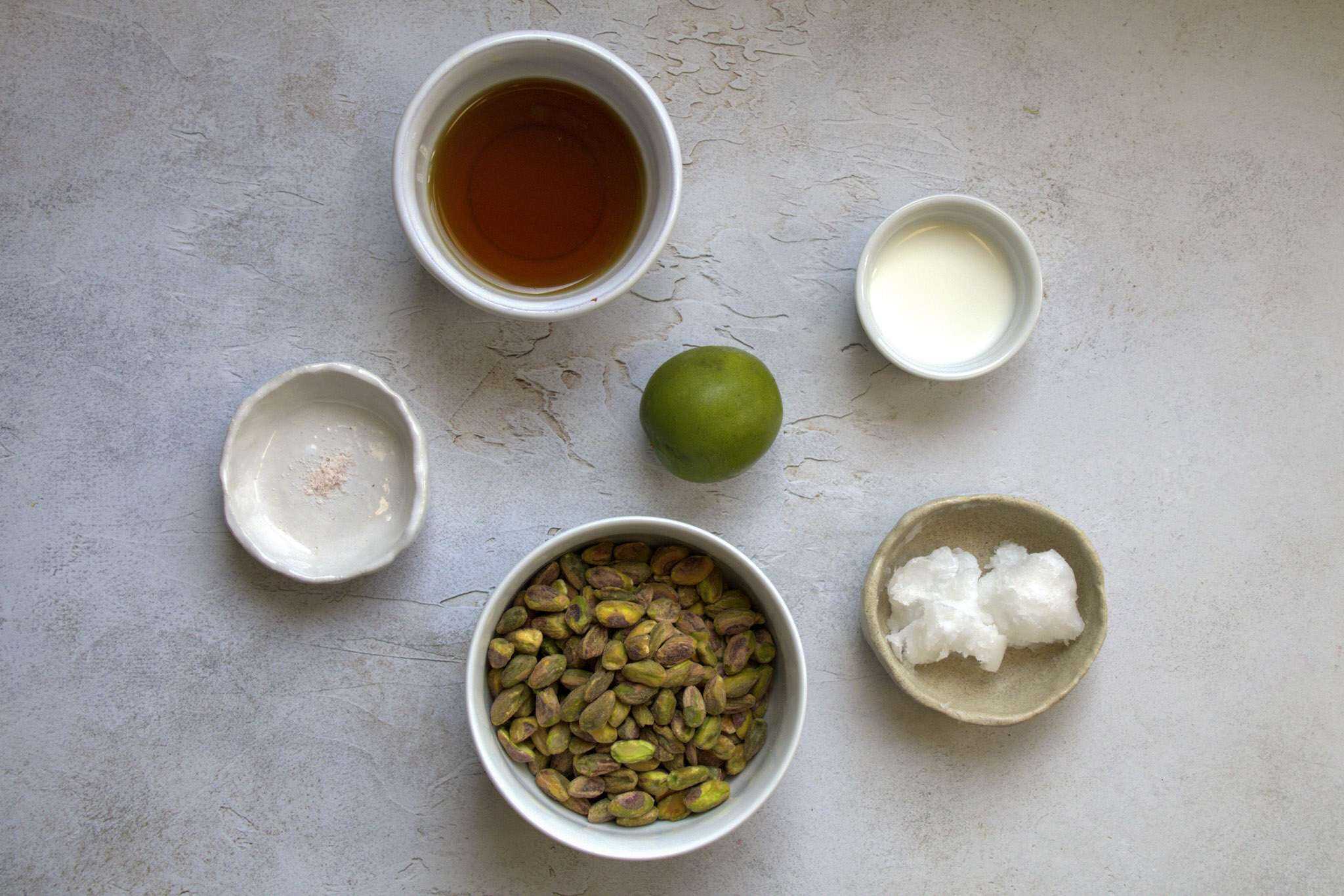 All ingredients for pistachio lime cream are displayed, including pistachios, coconut oil, fine sea salt, maple syrup. a lime and milk of choice (I chose nut milk)