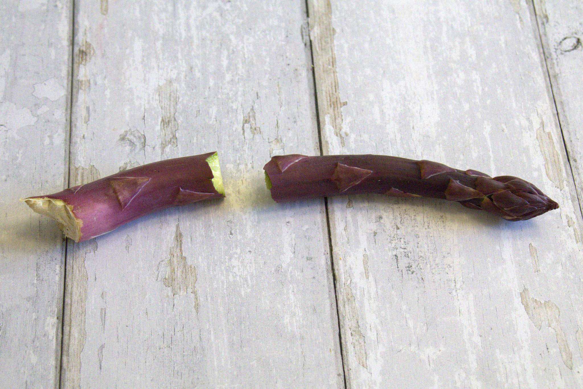 a purple asparagus spear with the tough end broken off is displayed on a white wooden surface