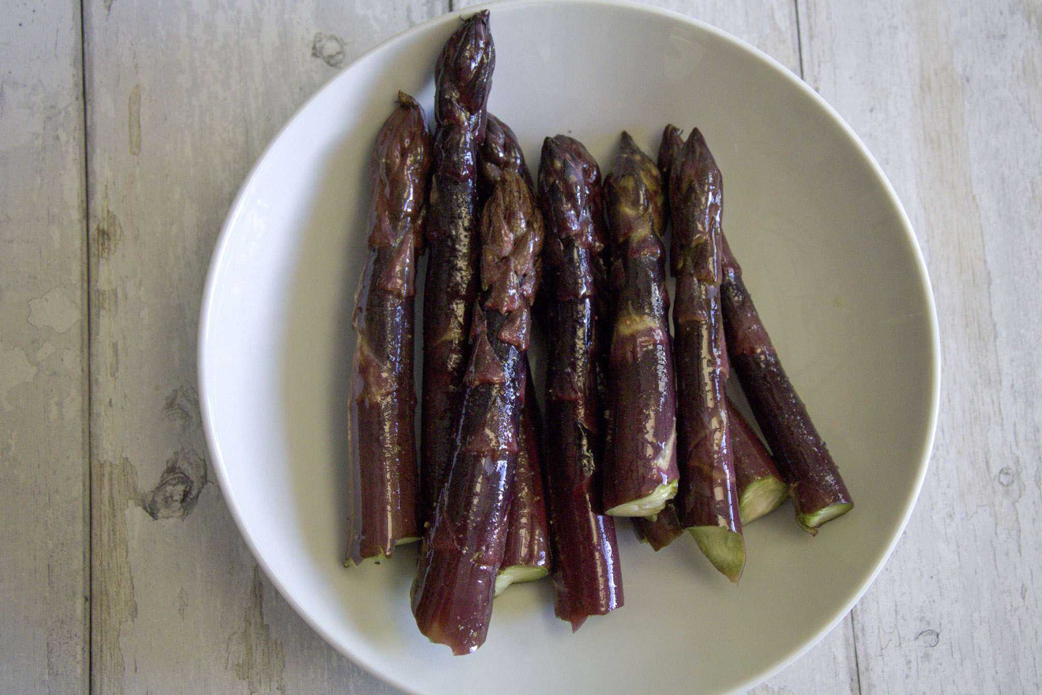 purple asparagus spears coated with extra virgin olive oil and sprinkled with salt and pepper in a white bowl