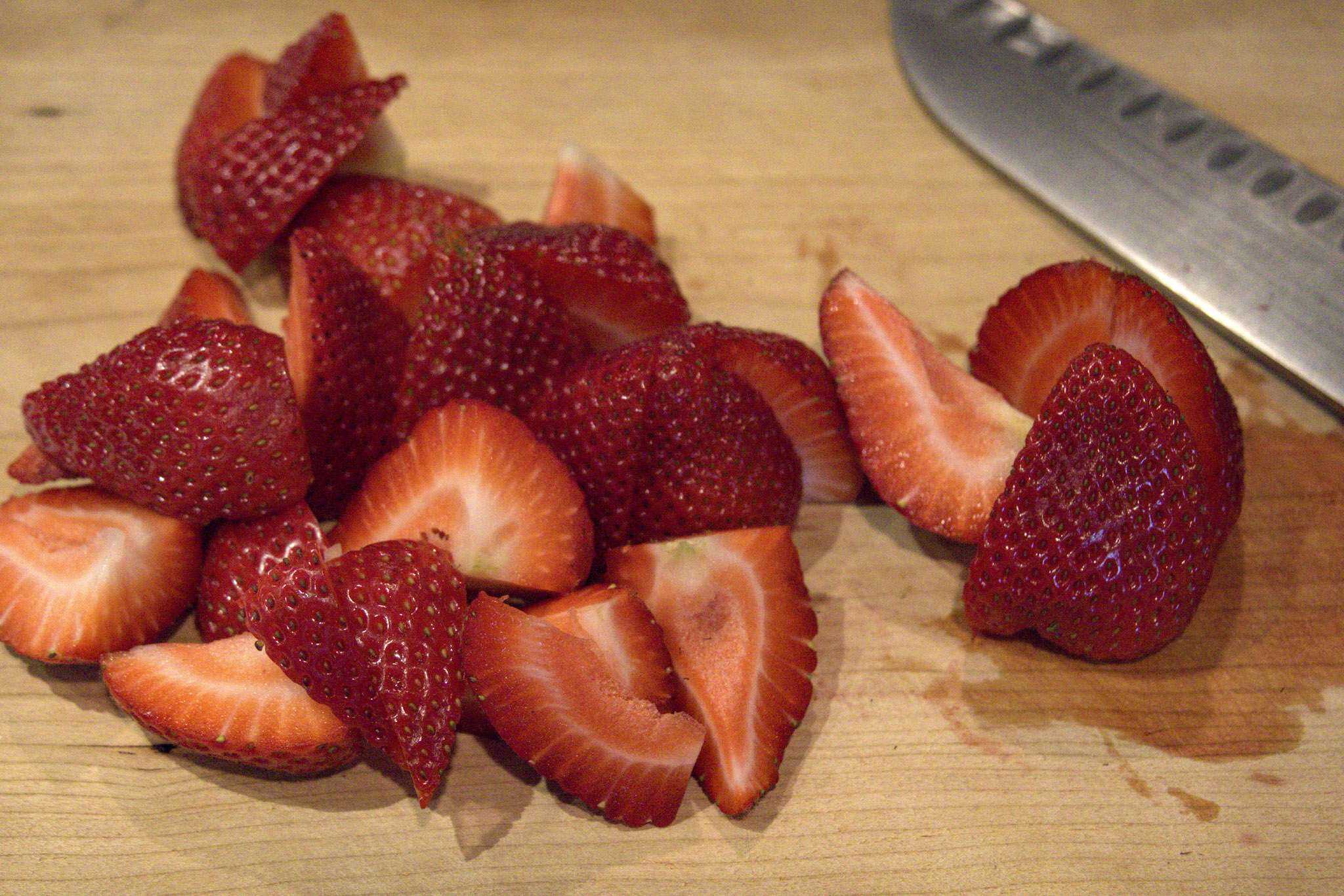 Cut strawberries are on a cutting board along with a knife