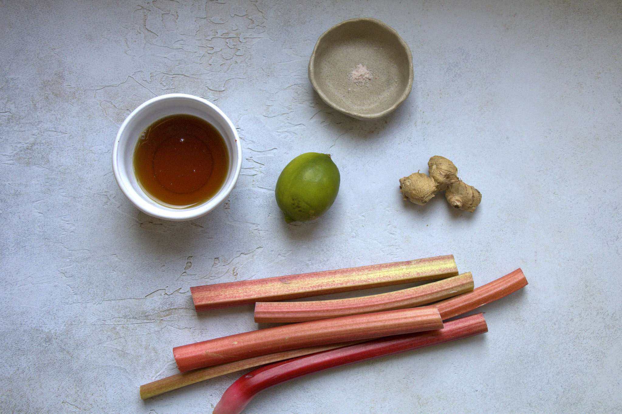 All ingredients for refined sugar free rhubarb compote are displayed, including rhubarb, lime, ginger, maple syrup and fine sea salt