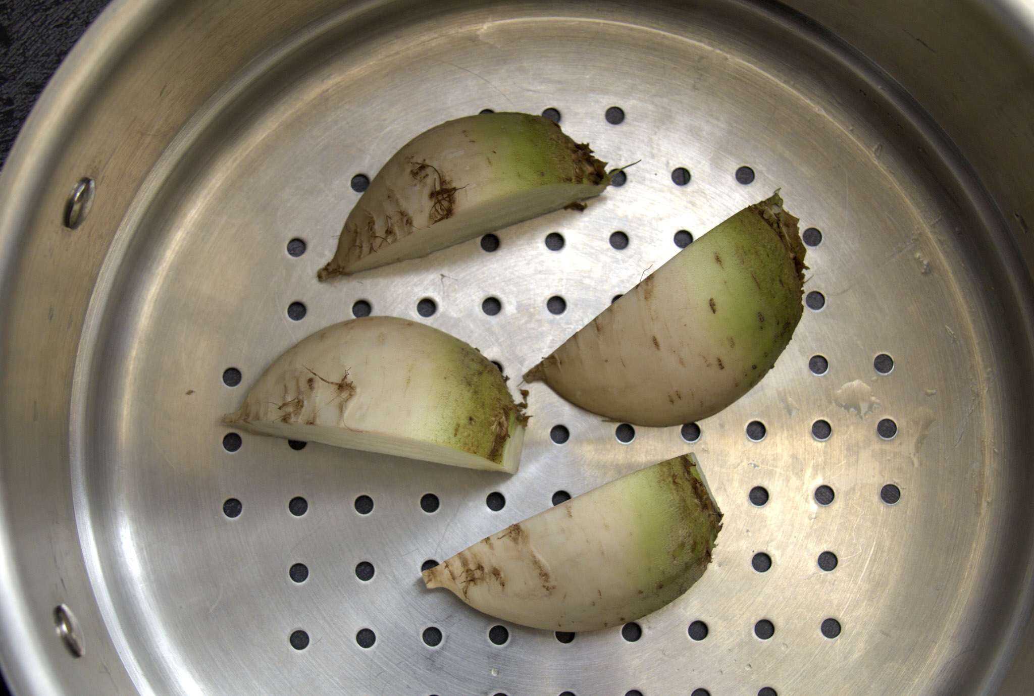 white beets cut into quarters are sitting in a steamer basket