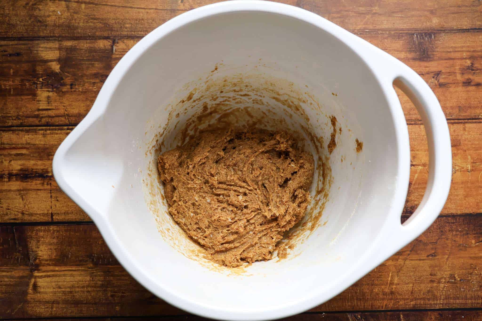 the dough for delicious gluten-free chocolate chip macadamia cookies (without the nuts and chocolate chips mixed in) is displayed in a white bowl, which is placed on a wooden surface