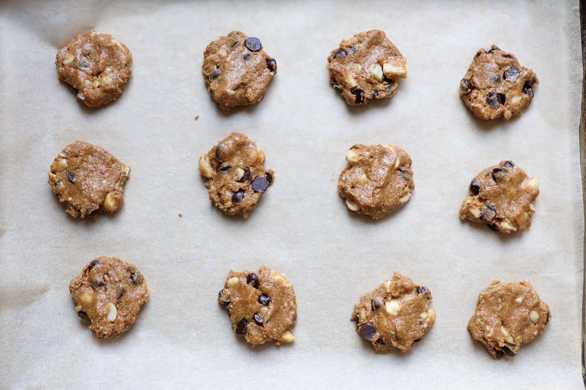 gluten free chocolate chip macadamia cookie dough balls on a parchment lined baking sheet - they were lightly flattened