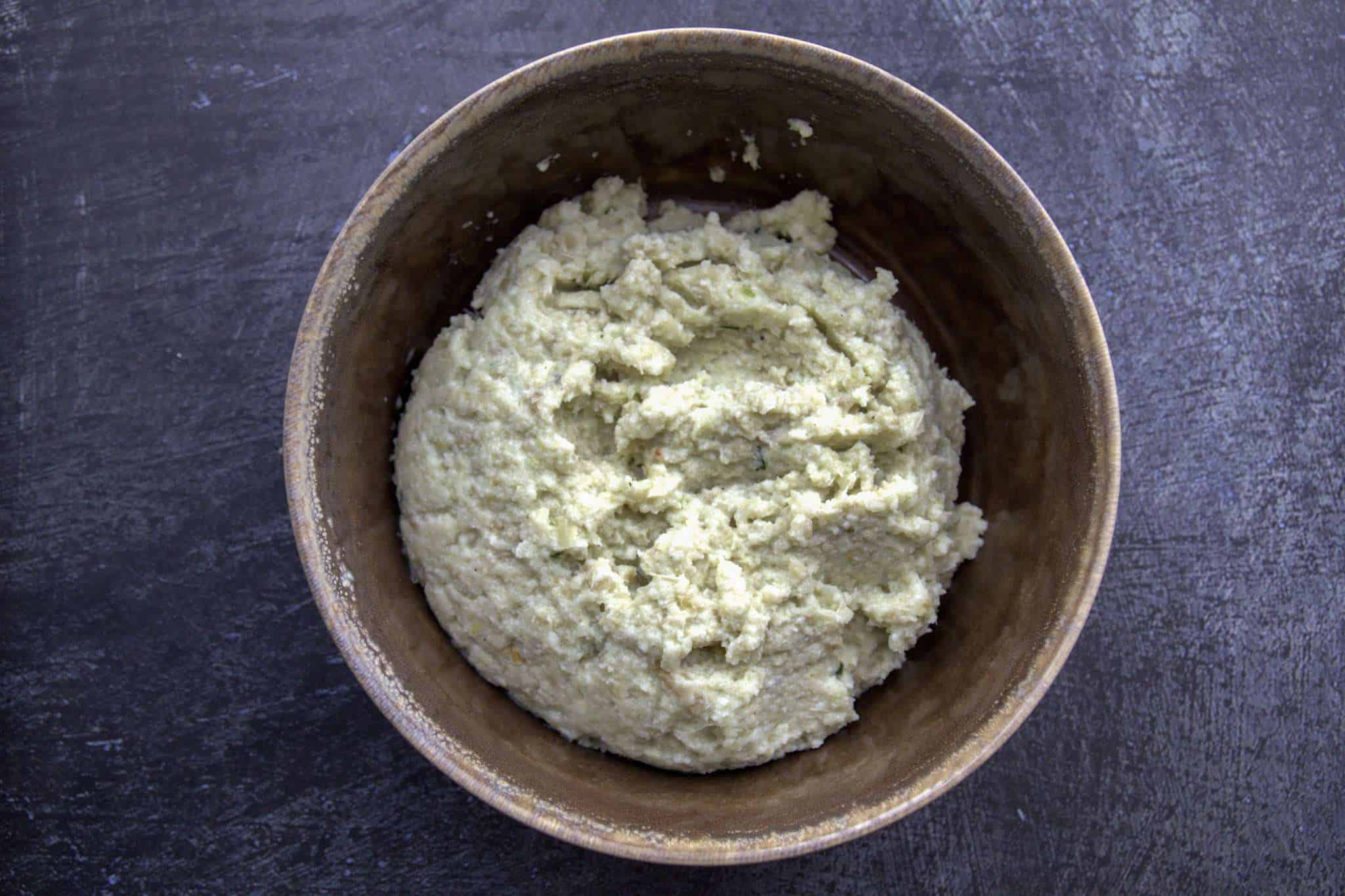 A brown bowl sitting on a dark grey concrete surface - the bowl contains the blended sunflower, beet and fennel puree