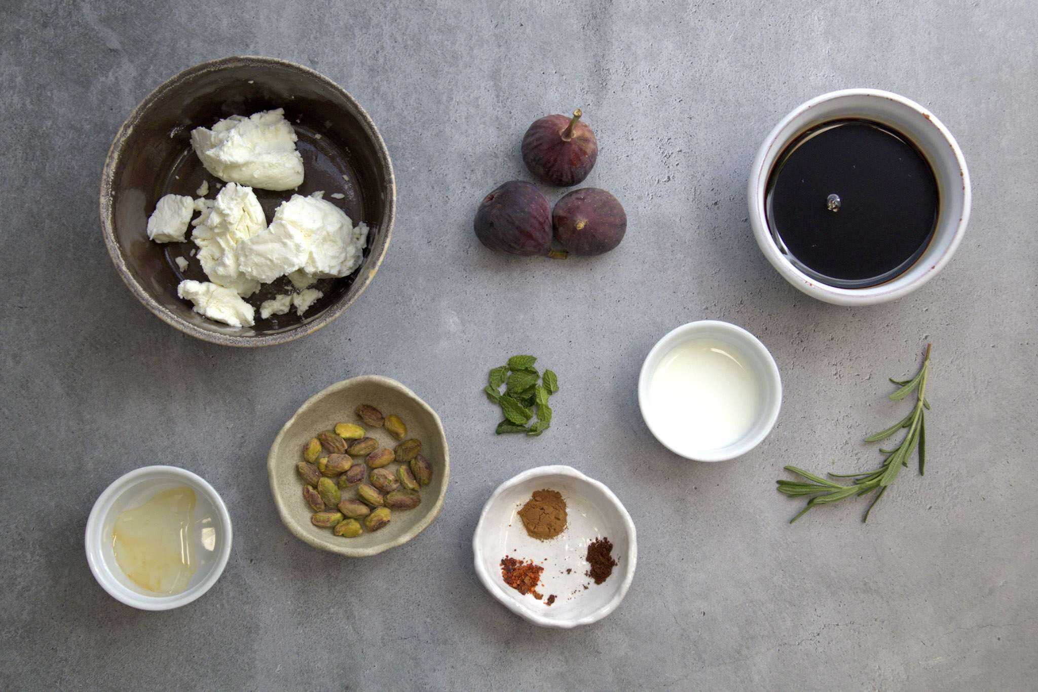 Ingredients for fig and goat cheese appetizer, including goat cheese, figs, pistachios, mint leaves, balsamic vinegar, rosemary, goat milk, honey, aleppo pepper, cinnamon and cloves