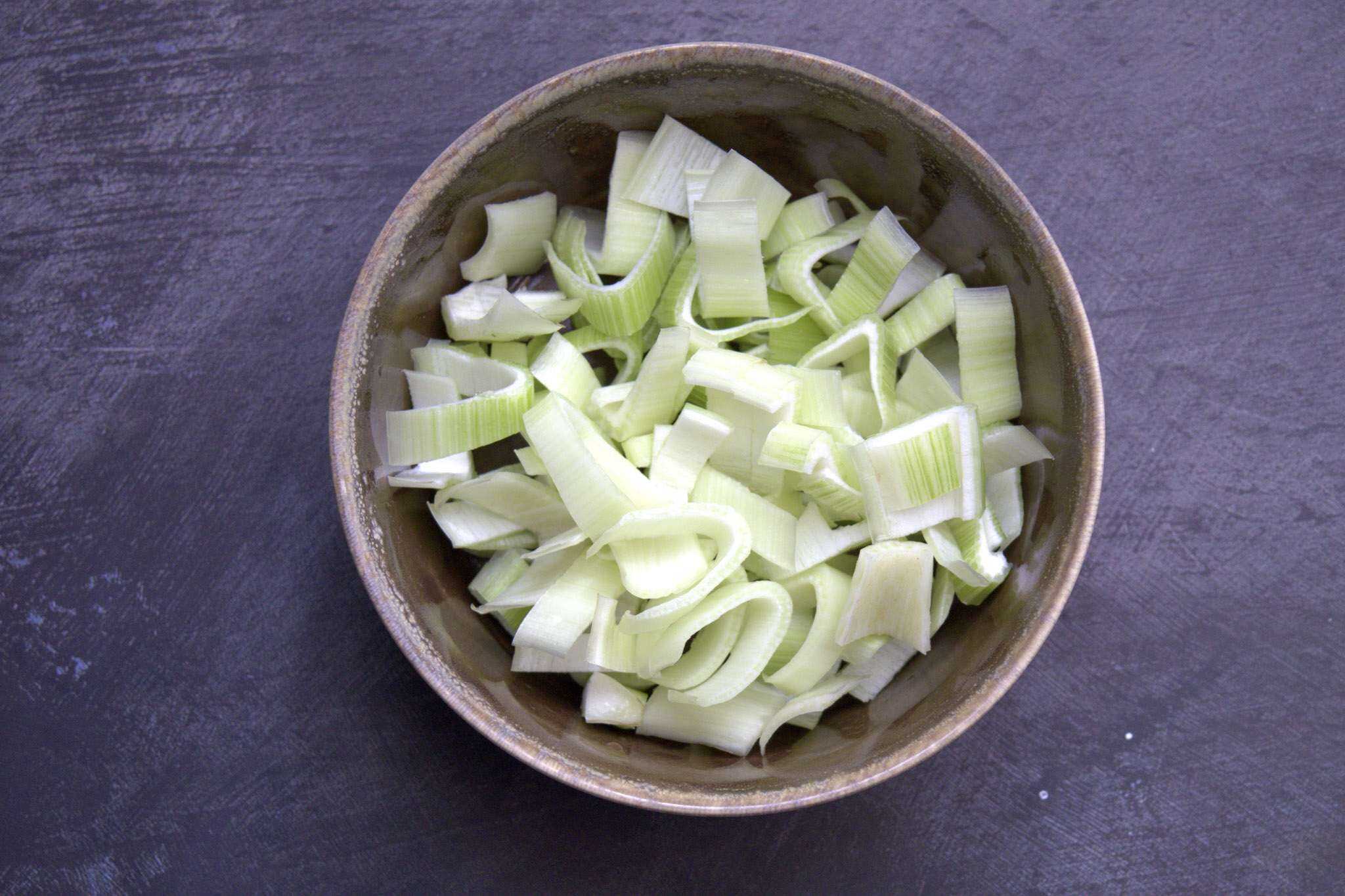 A brown bowl containing chopped fennel is sitting on a dark grey concrete style surface