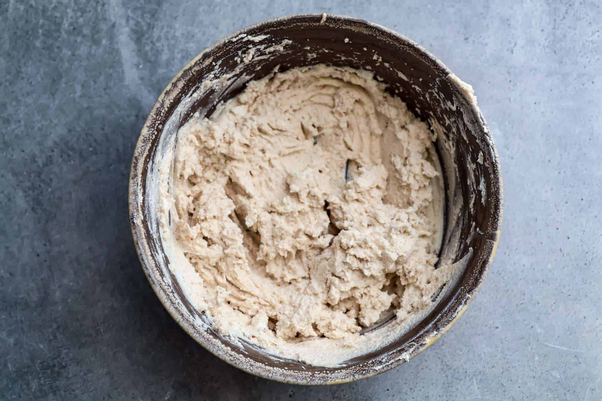 A rustic brown bowl on a grey concrete style background, holding goat cheese blended with cinnamon, clove and aleppo pepper