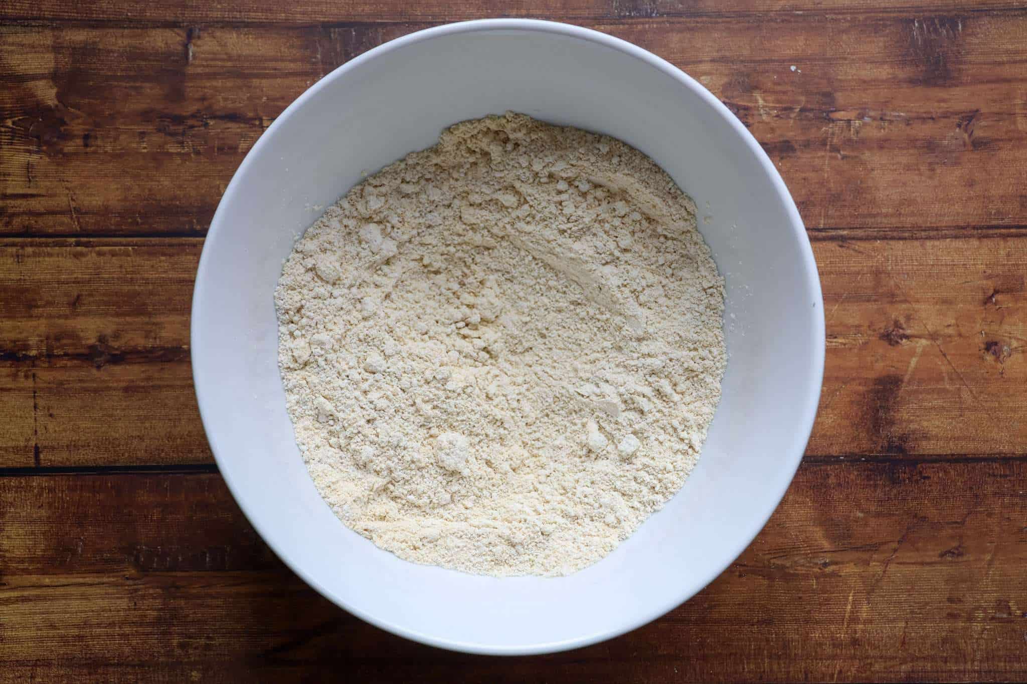 the dry ingredients for delicious gluten-free chocolate chip macadamia cookies are displayed in a white bowl, which is placed on a wooden surface