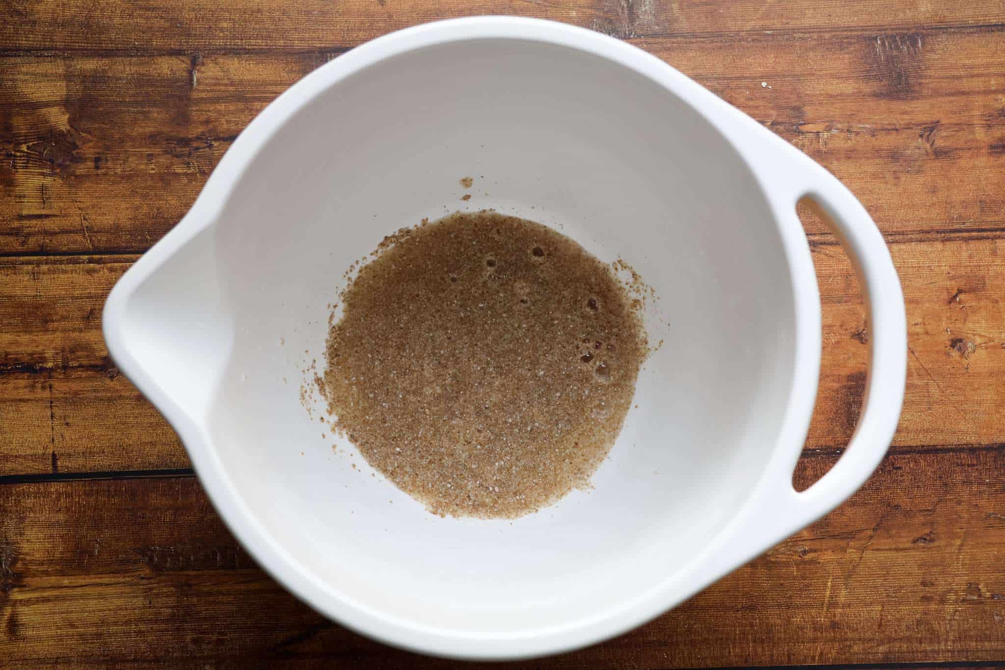 A white bowl with ground chia soaking in water is displayed on a wooden surface