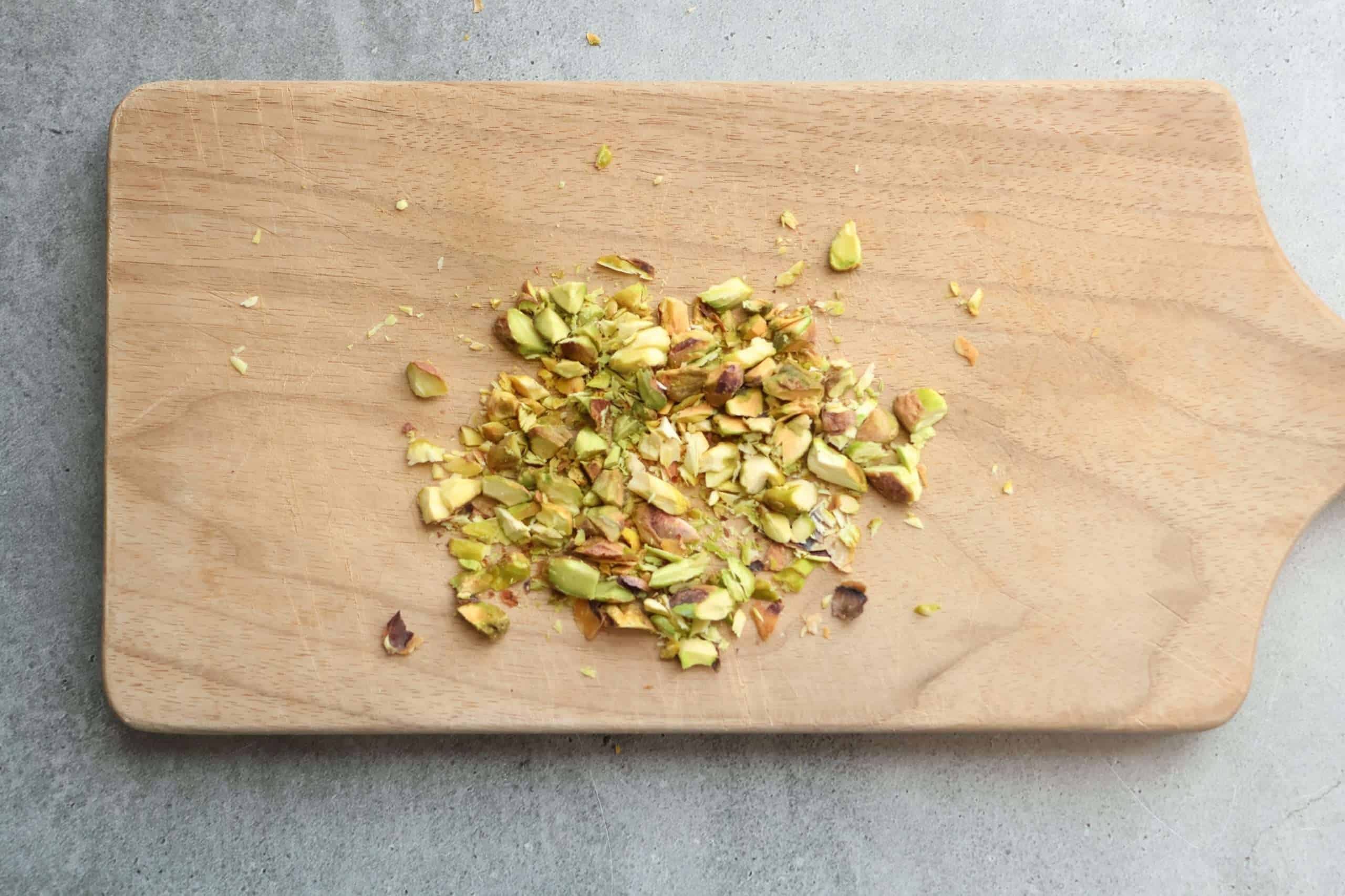 A small wooden board with chopped pistachios