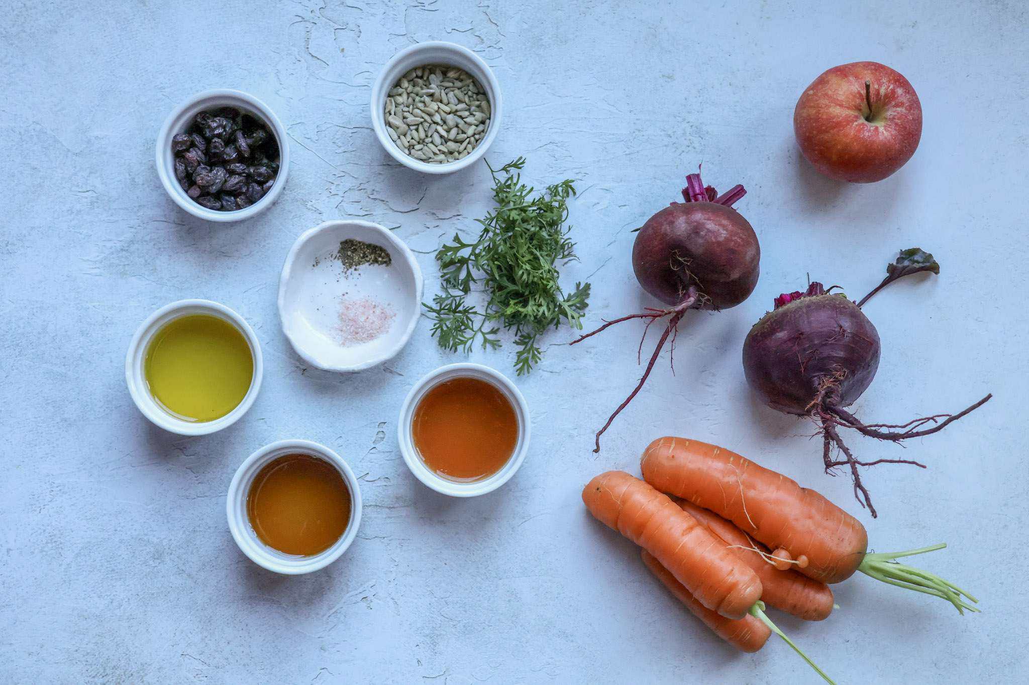 All ingredients for crunchy beet and carrot slaw with apple are displayed on a concrete style background