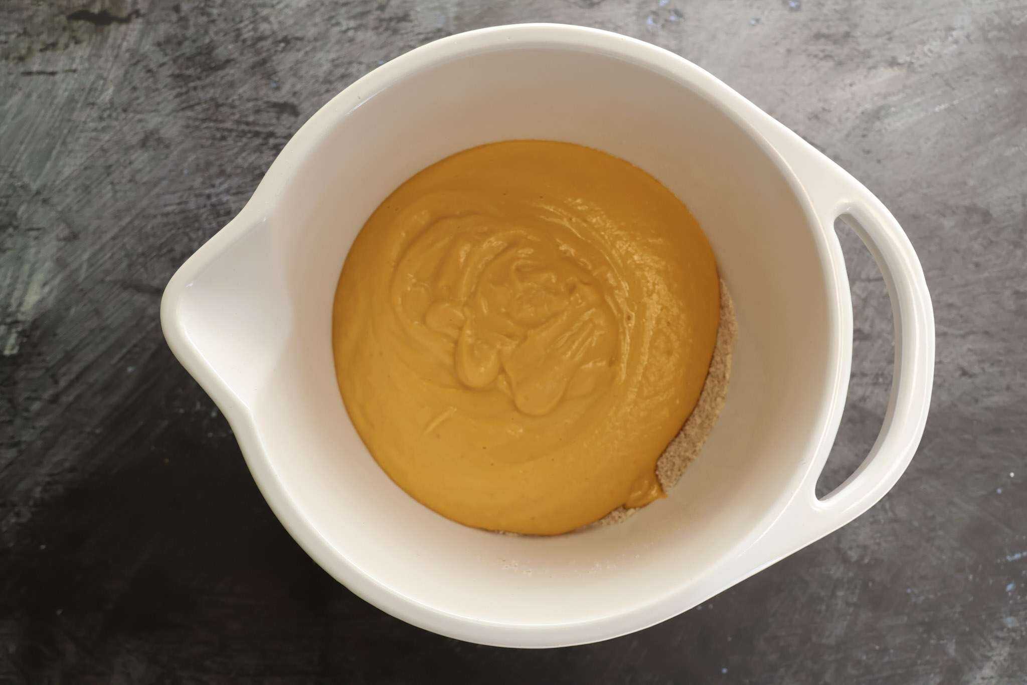 A white mixing bowl with the dry and wet ingredients for Soft and Fluffy Pumpkin Bars (with White Beans and a Healthy Twist) prior to whisking them all together