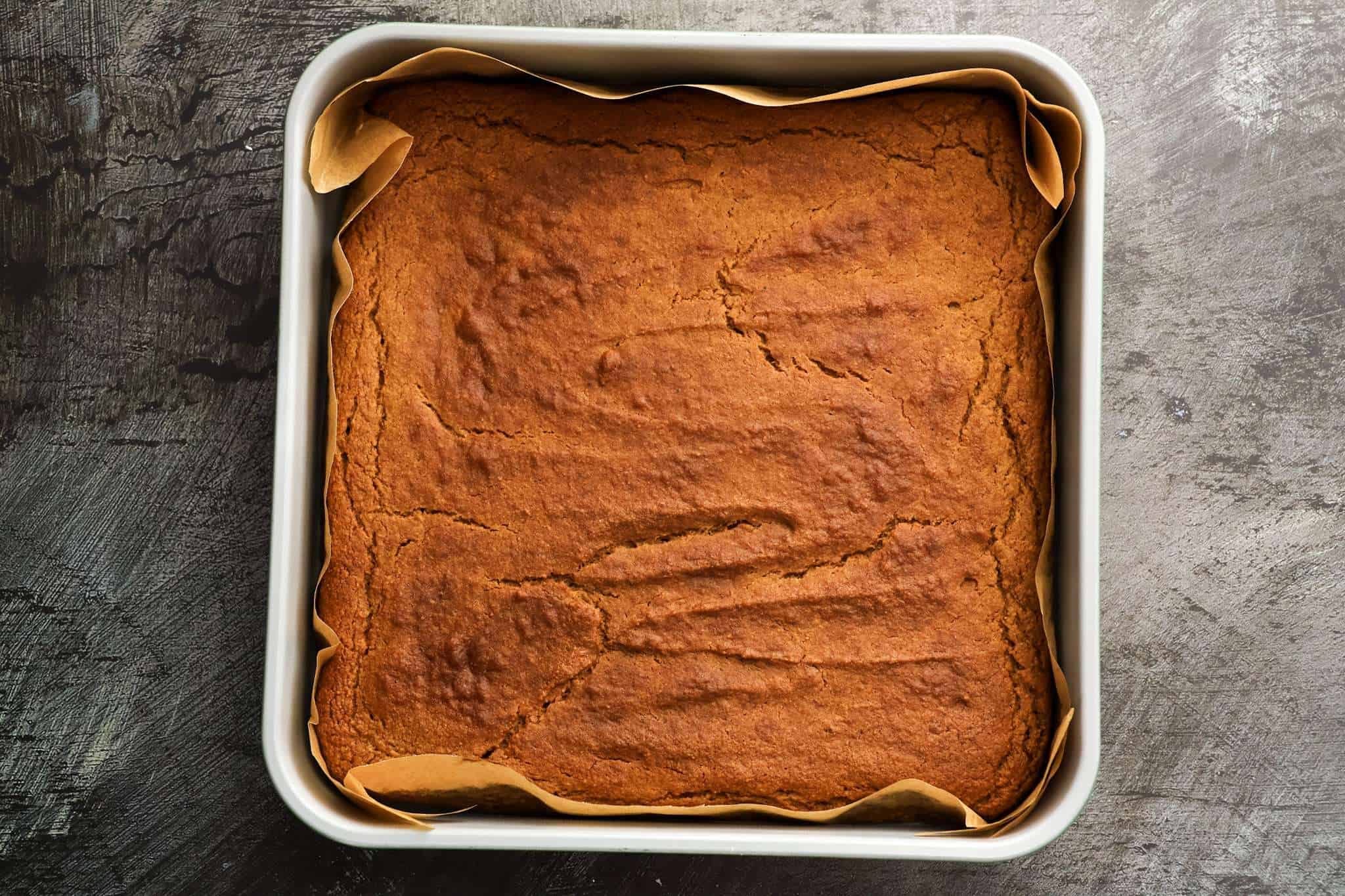 A 9x9 parchment lined baking pan with baked pumpkin bars