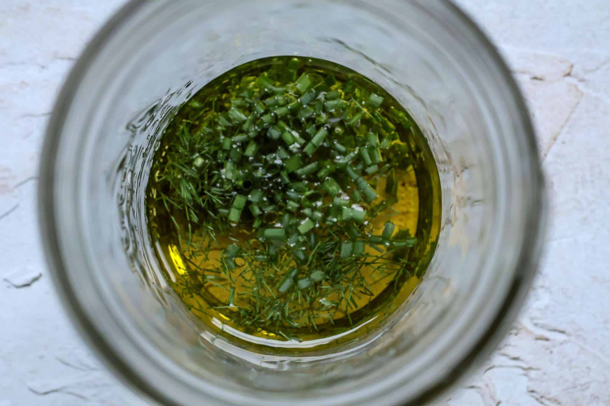A jar with extra virgin olive oil, fennel fronds and chopped chives