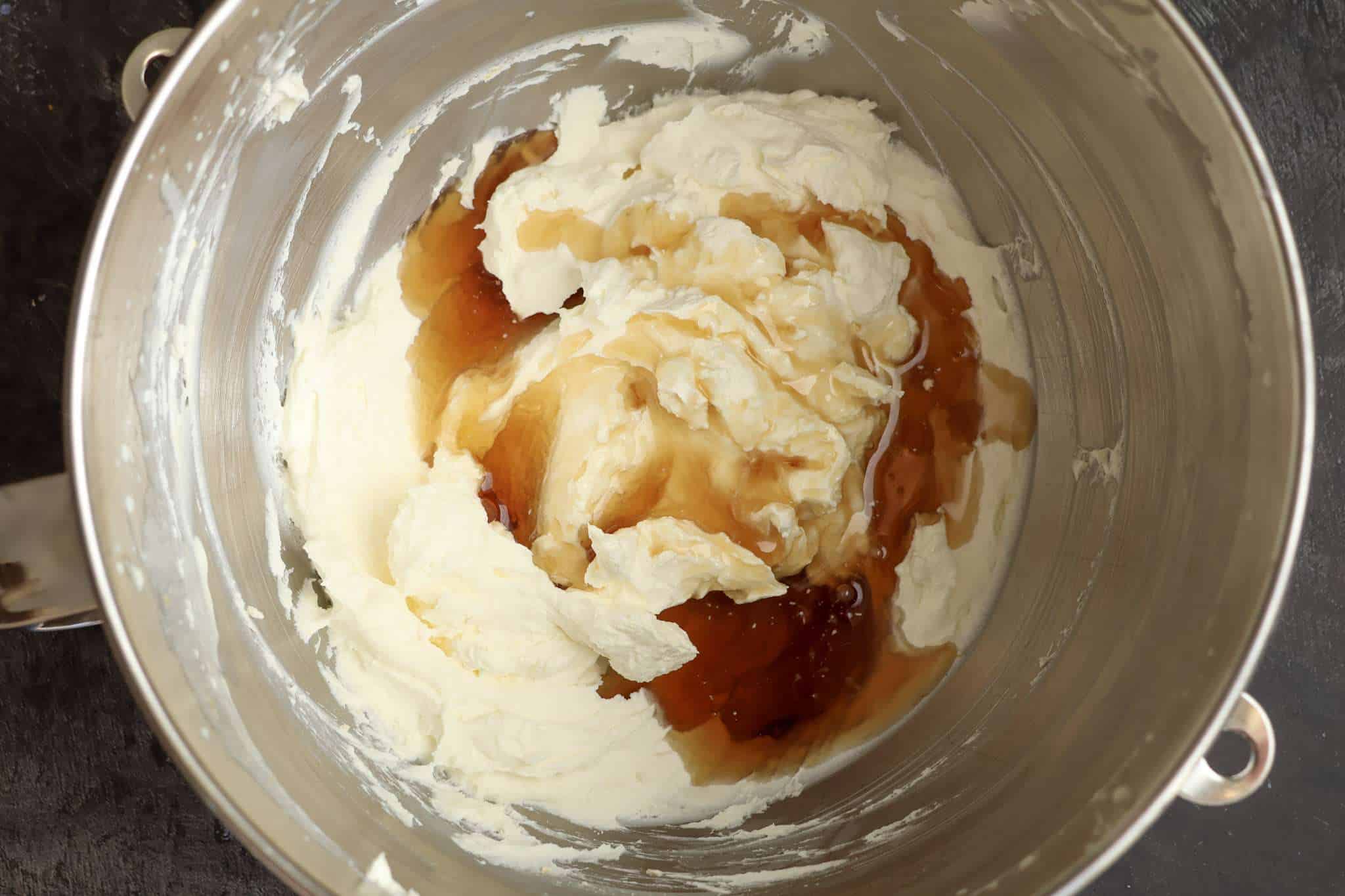 Whipped orange mascarpone frosting in a mixer bowl with the maple syrup just added