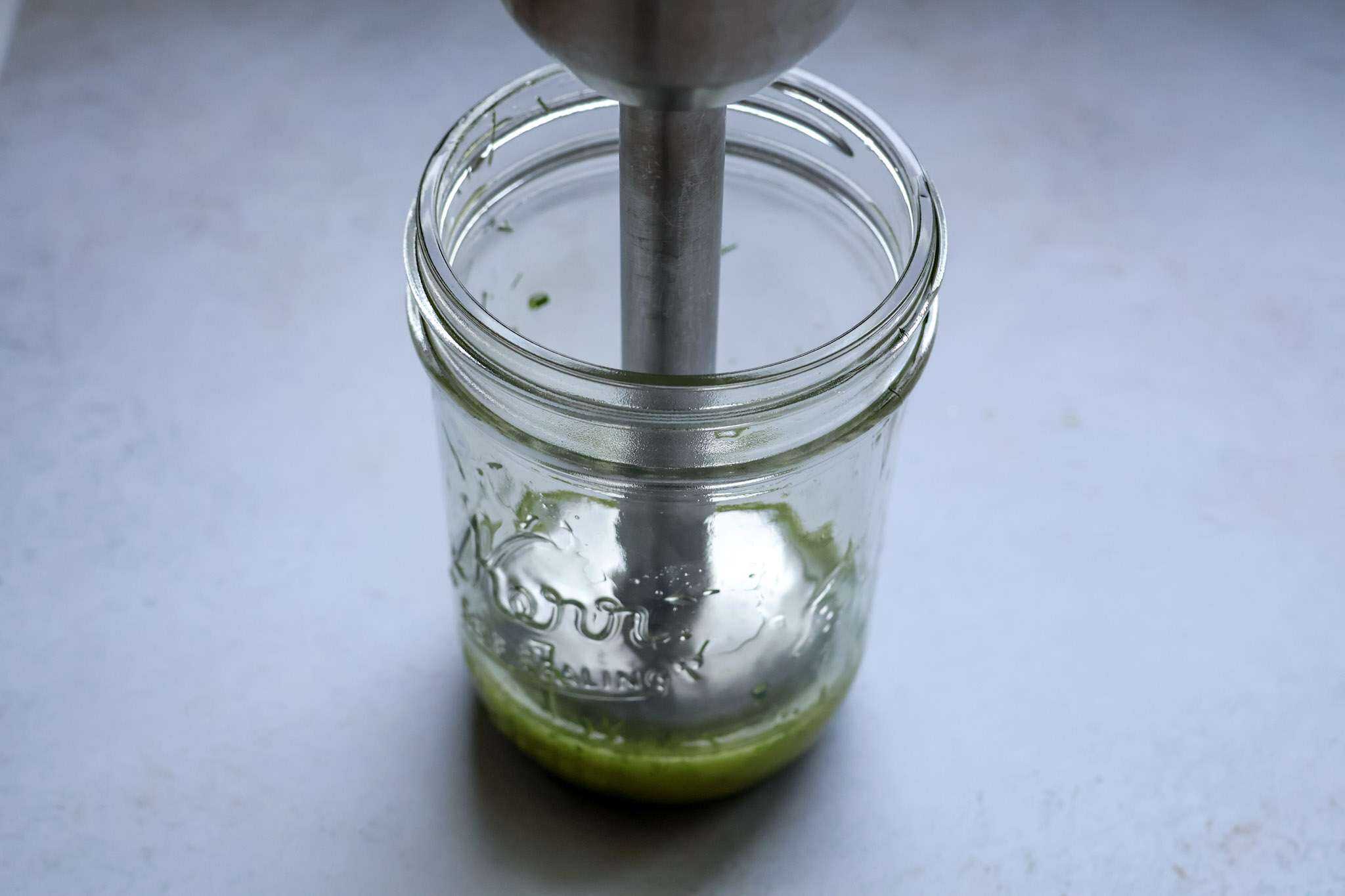 A small jar with extra virgin olive oil, chives and fennel fronds with an immersion blender in it