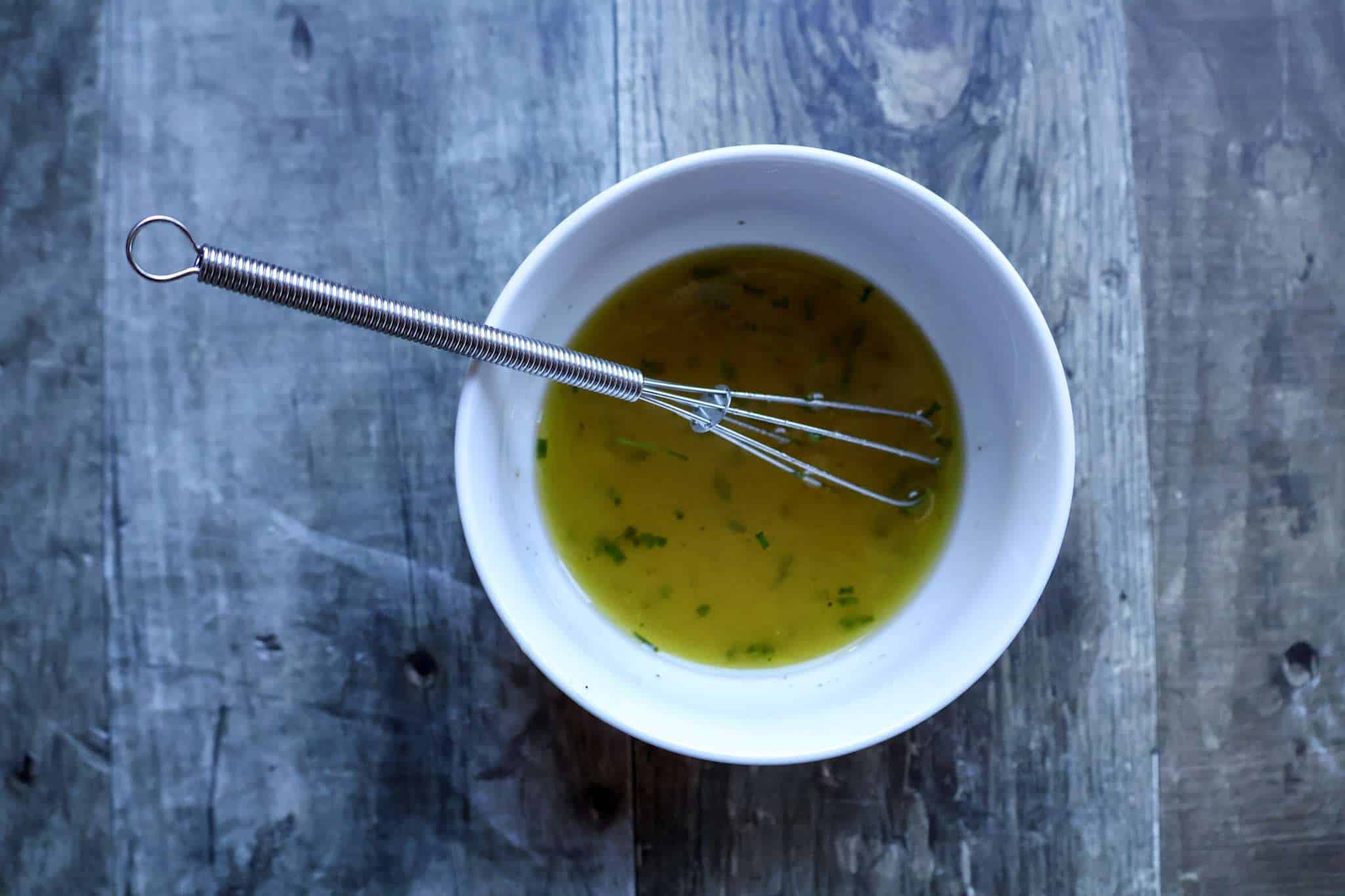 A white bowl with a lemon vinaigrette and a small whisk resting inside