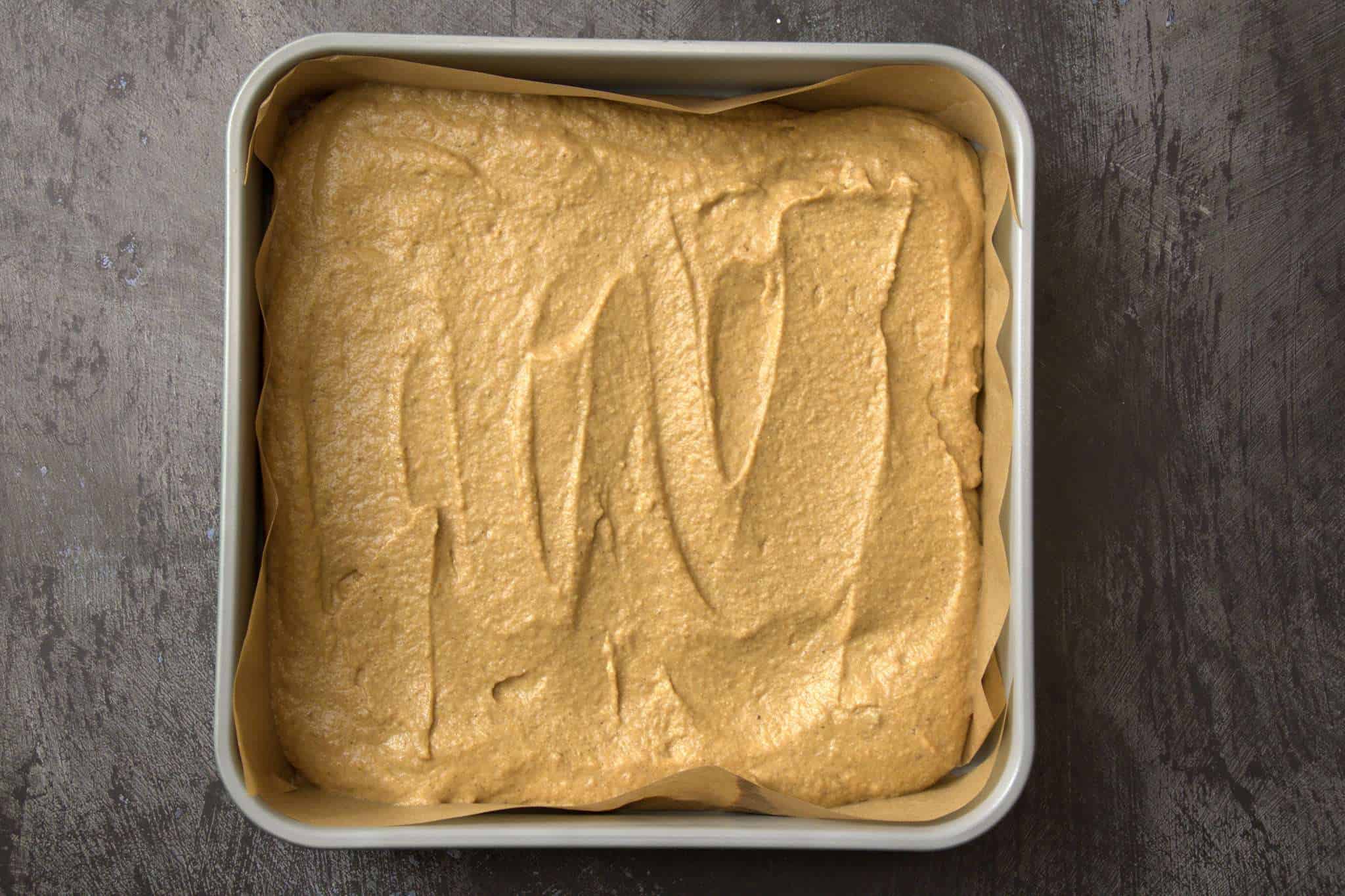 A 9x9 parchment lined pan with pumpkin bar batter ready to go into the oven