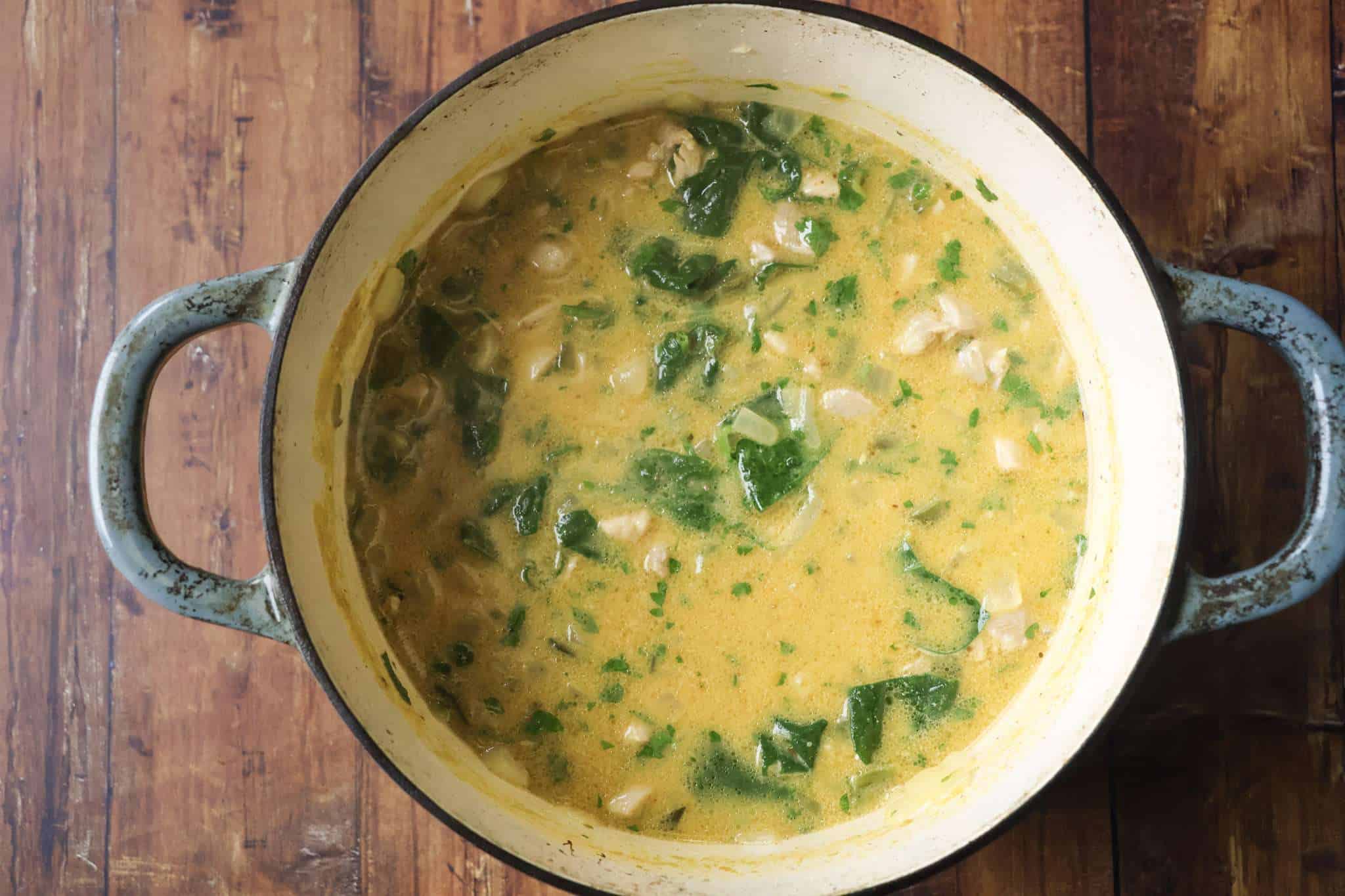 a Dutch oven with creamy chicken and pumpkin chili with coconut milk and spinach added