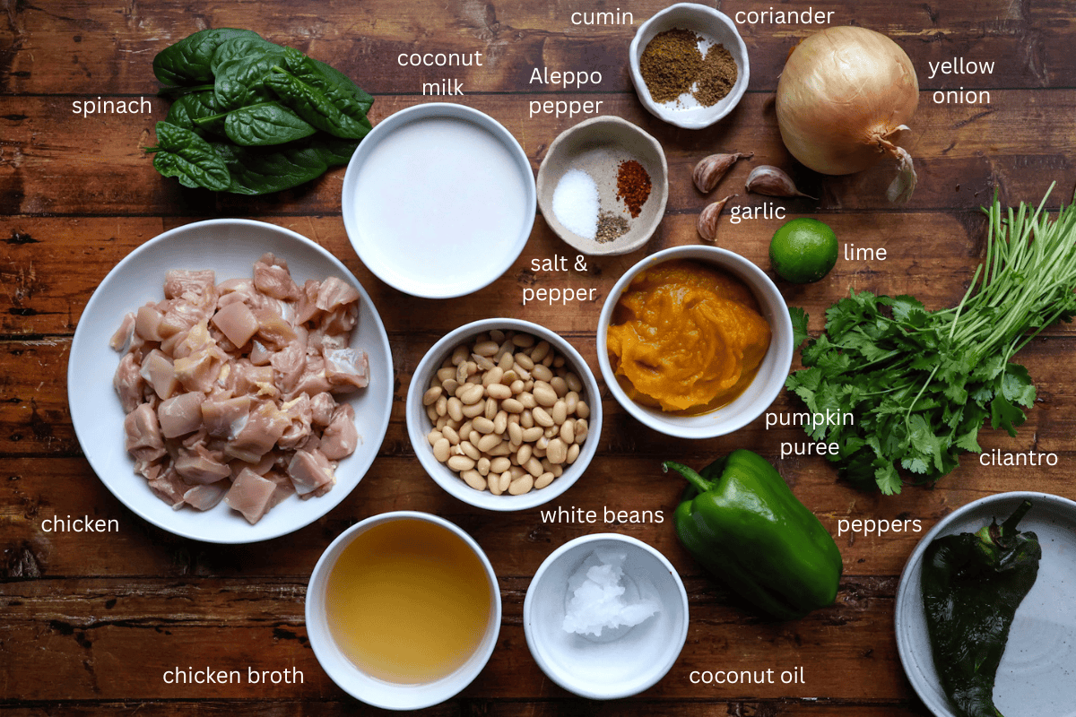 All ingredients (labeled) for creamy pumpkin and chicken chili with coconut milk are displayed on a wooden surface