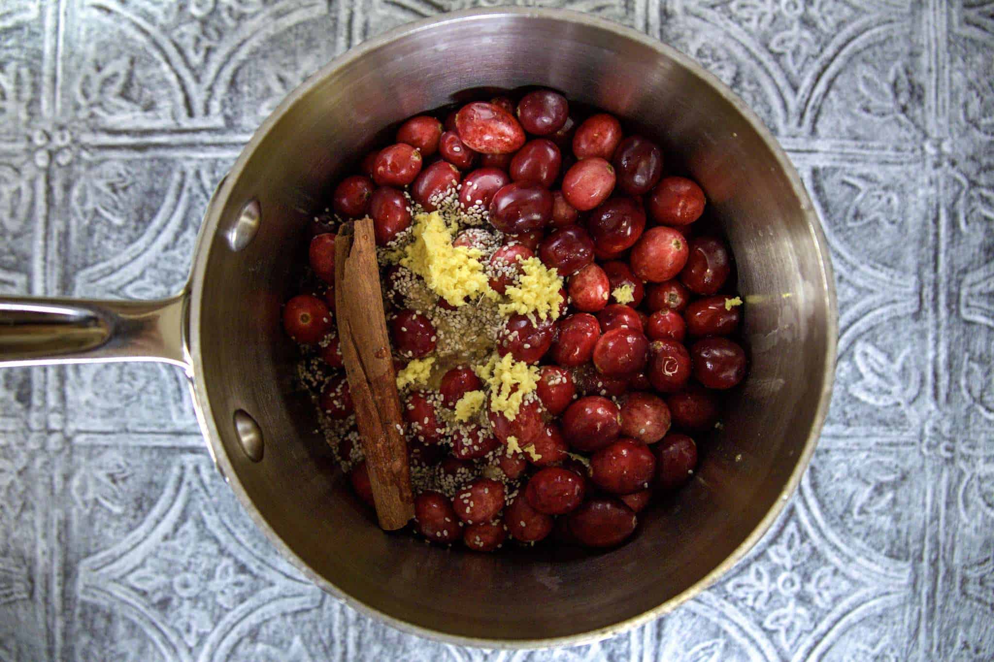 A small pot containing all ingredients for cranberry chia jam with orange and ginger