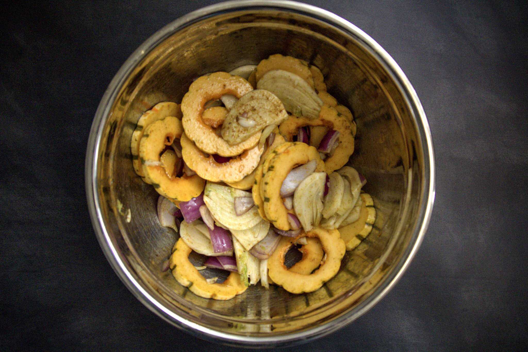 A bowl with seasoned delicata squash rings, sliced fennel, and red onion