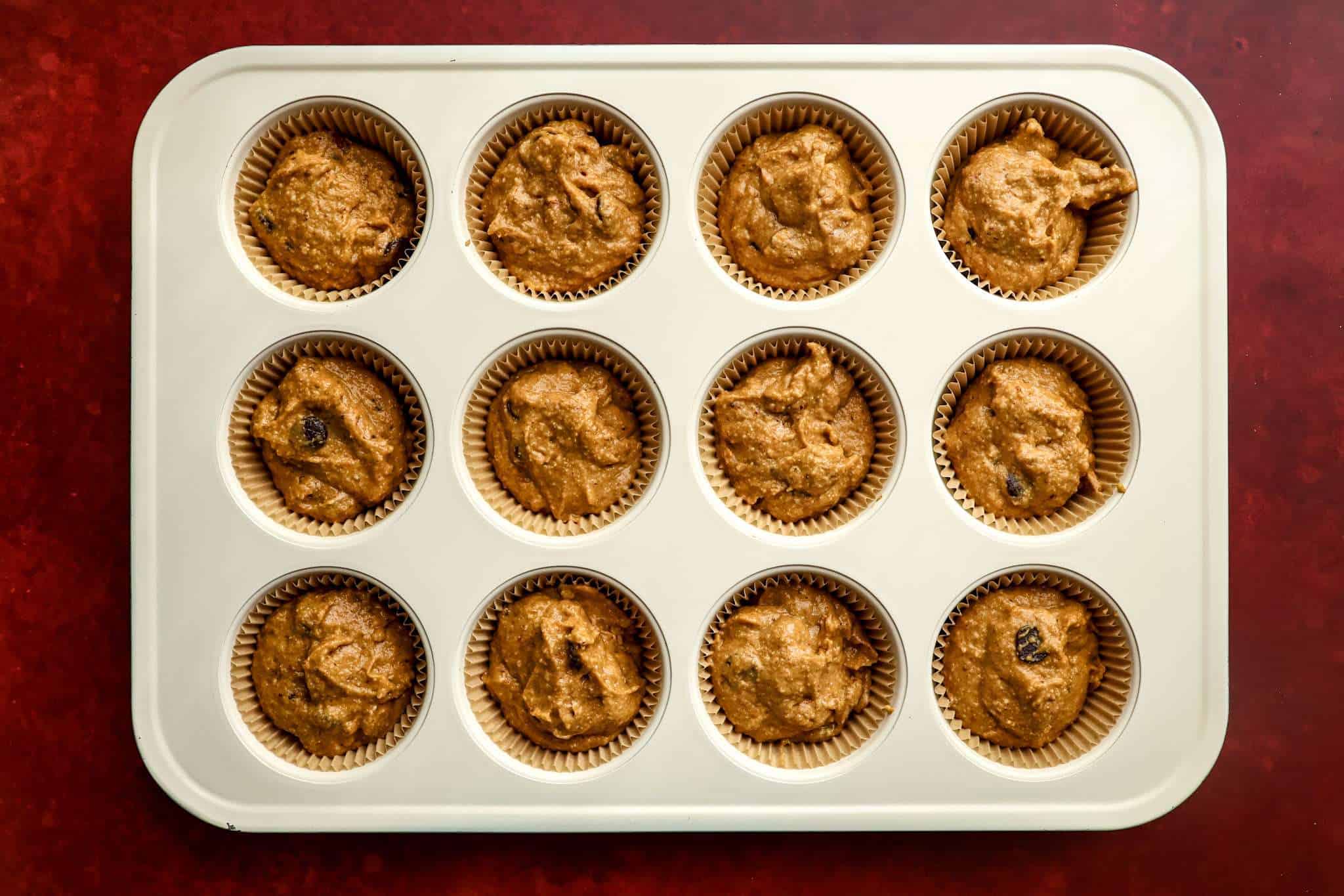 a muffin tin on a red surface - the tin is lined with cupcake liners and filled with batter for tender gluten-free pumpkin muffins