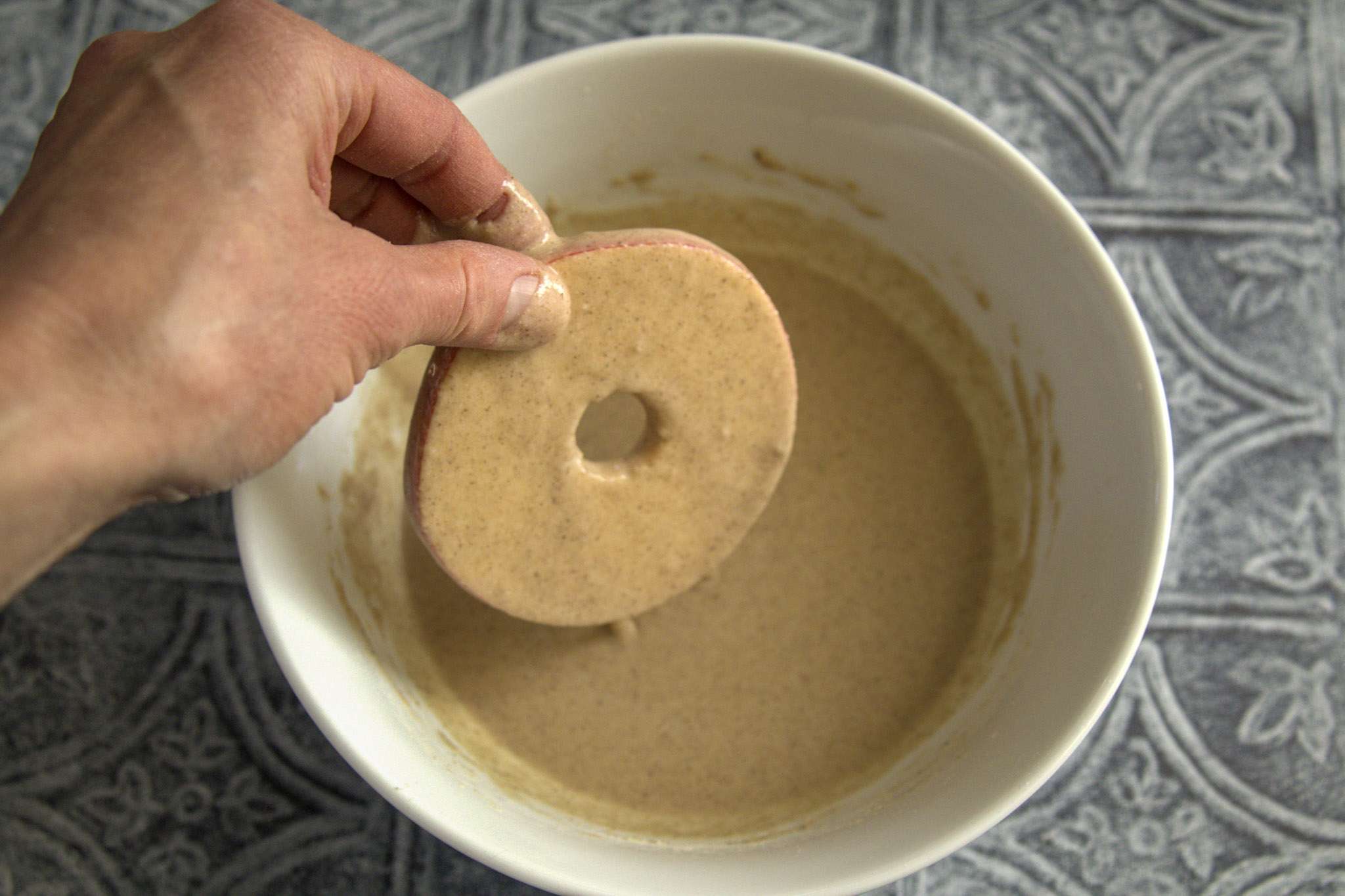 a white bowl with apfelringe batter and a hand dipping an apple slice into the batter