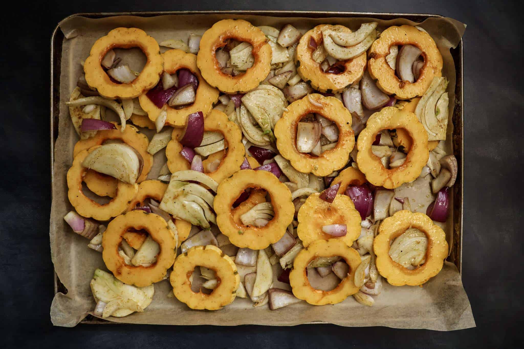 A baking sheet with ras el hanout seasoned delicata squash rings, sliced fennel, and red onion