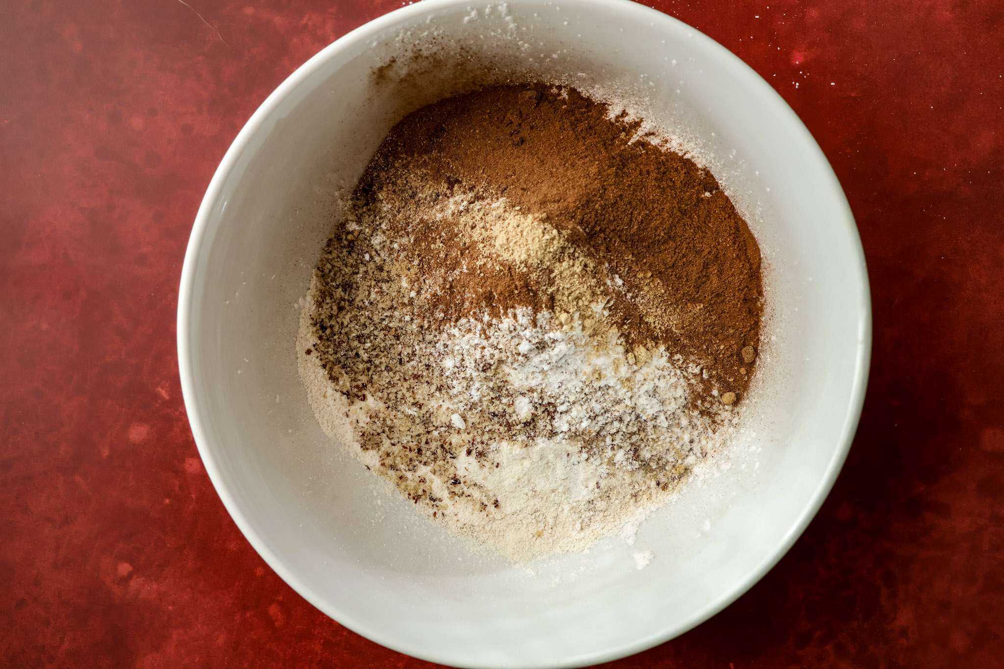 a white bowl on a red surface - the bowl contains all the dry ingredients for tender gluten-free pumpkin muffins