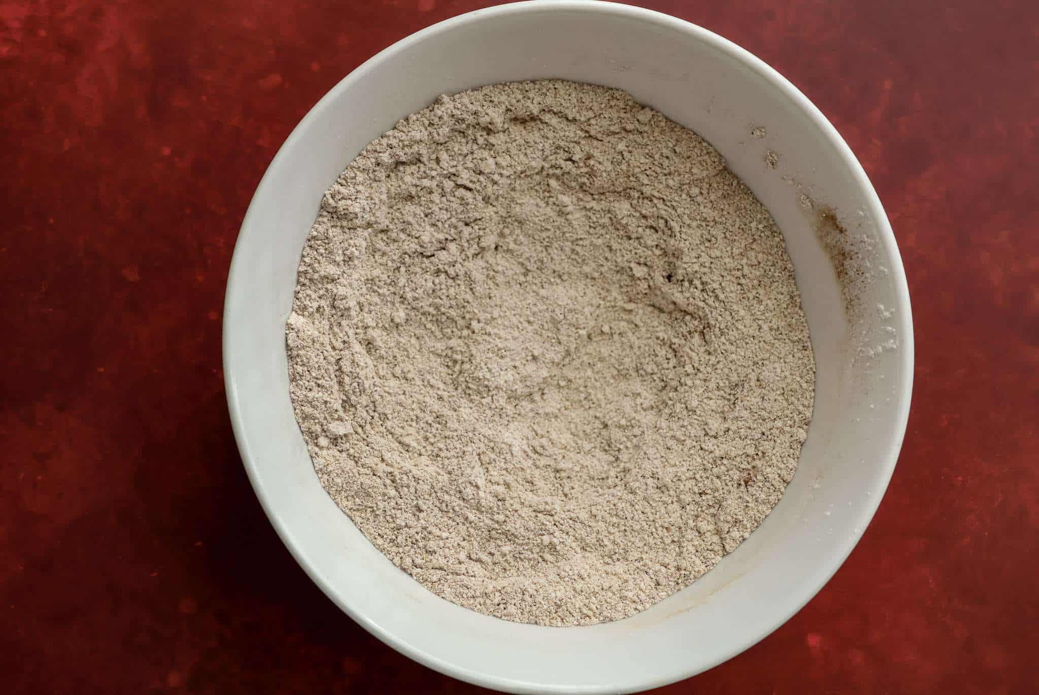 w white bowl on a red surface - the bowl contains the blended dry ingredients for tender gluten-free pumpkin muffins